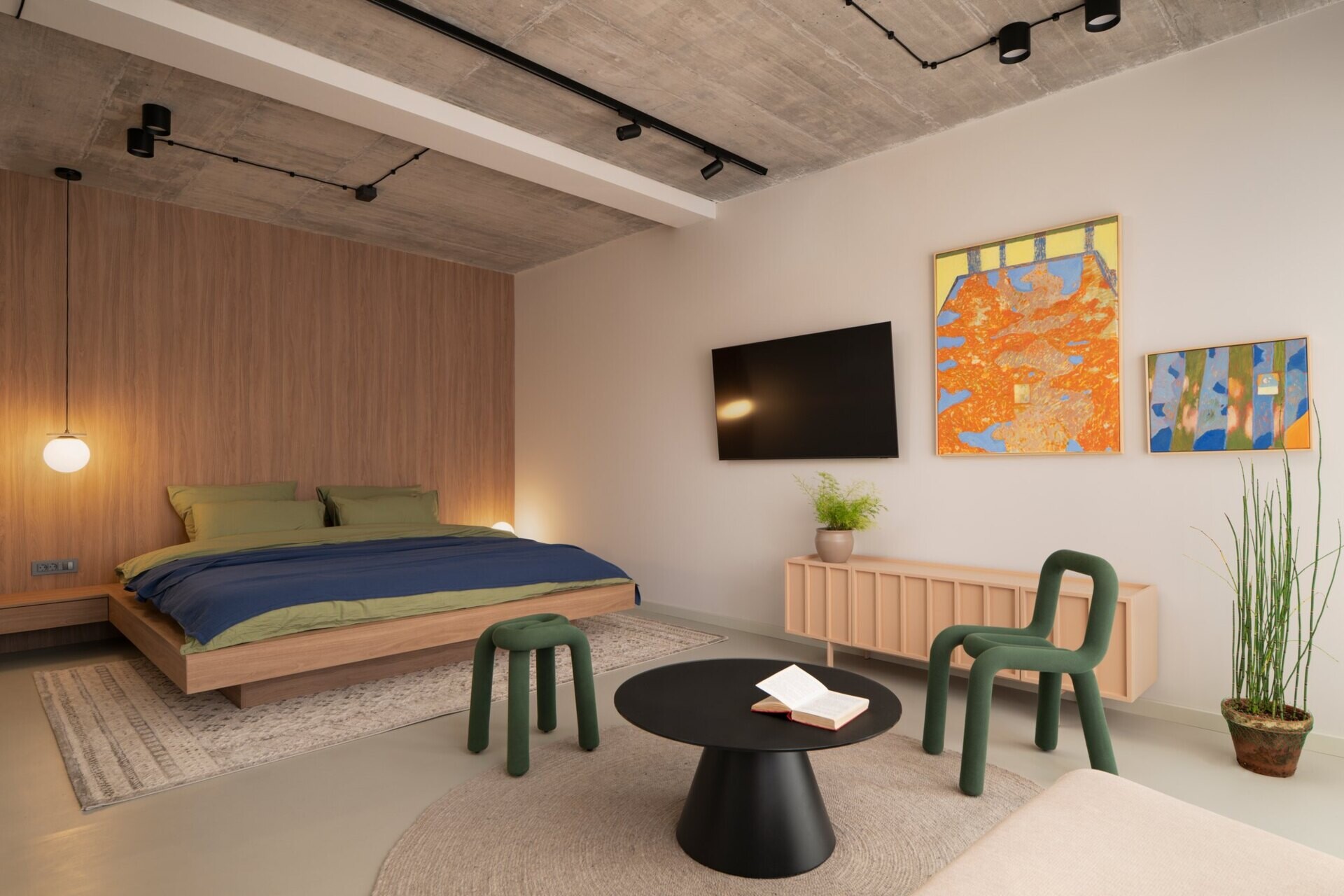 Explore Guest Bedroom A at Arc House in Istria, featuring a wood-panelled bed wall, green sculptural chairs, pink sideboard, colourful abstract art and blue and olive-green bedding.