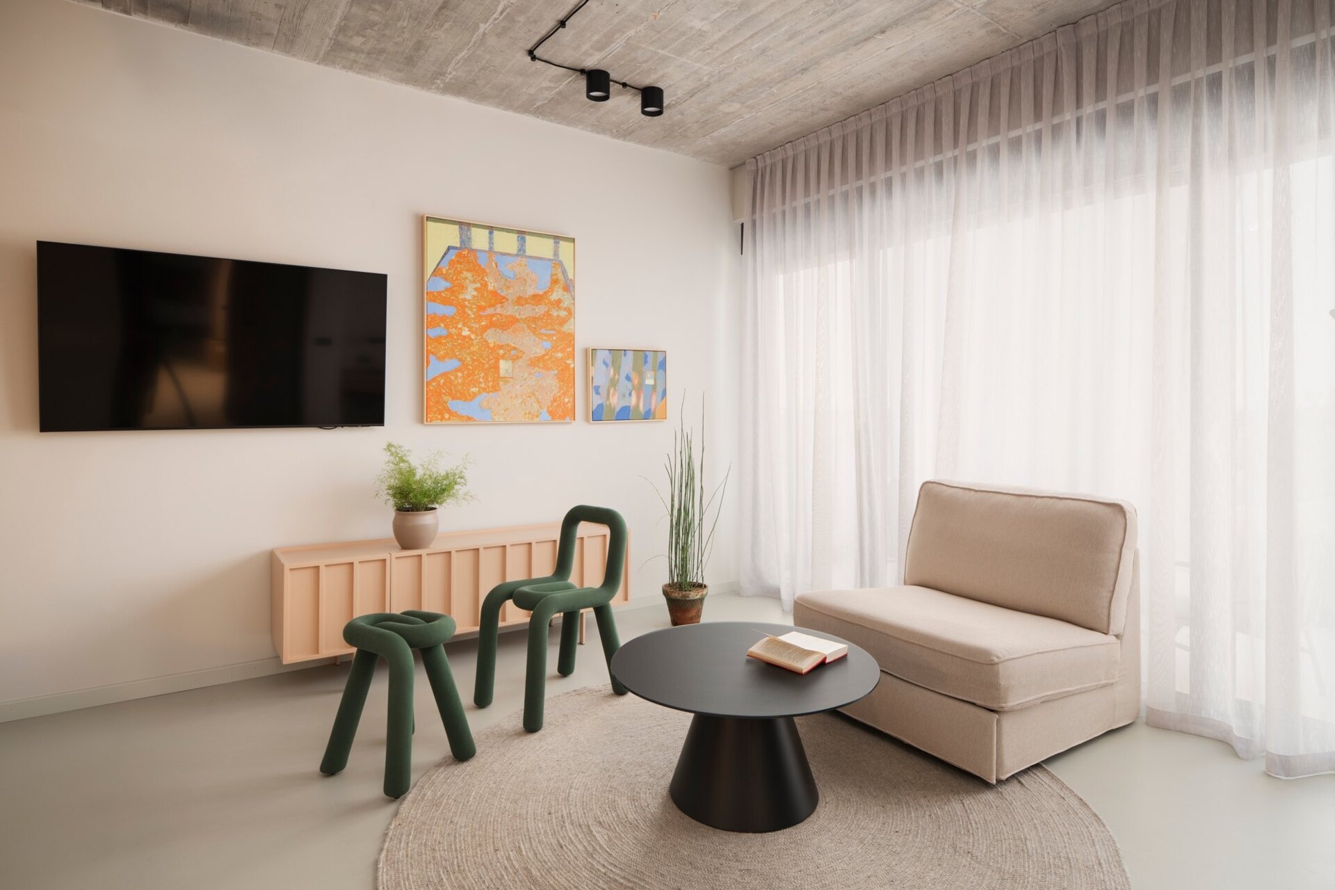 Explore Guest Bedroom A at Arc House in Istria, featuring a wood-panelled bed wall, green sculptural chairs, pink sideboard, colourful abstract art and blue and olive-green bedding.