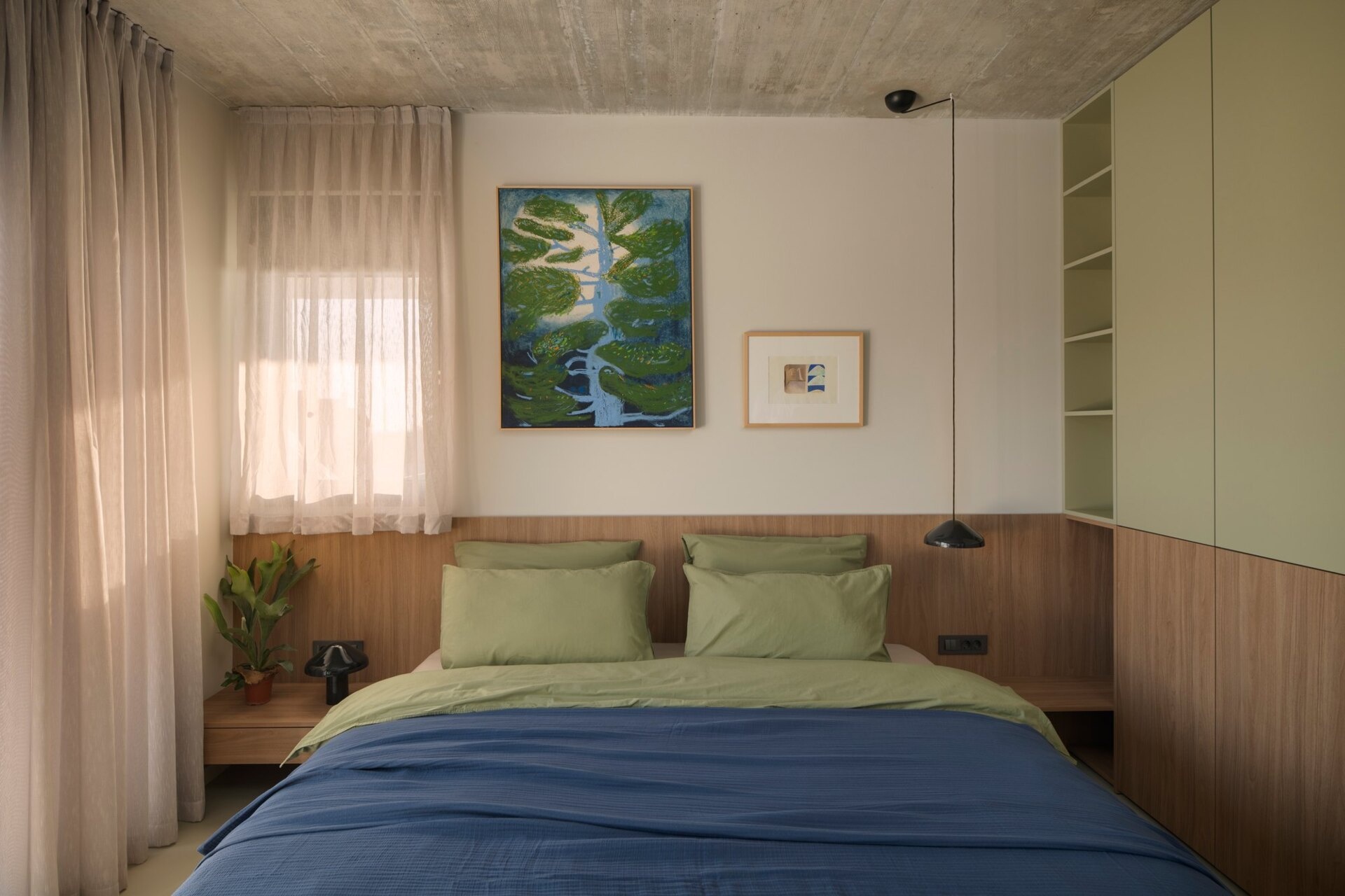 Take a look at a guest bedroom in Arc House, Croatia, featuring sage-green wardrobes, a timber headboard, blue and green bedding, open display shelves, indoor plants and a full-length arched mirror.