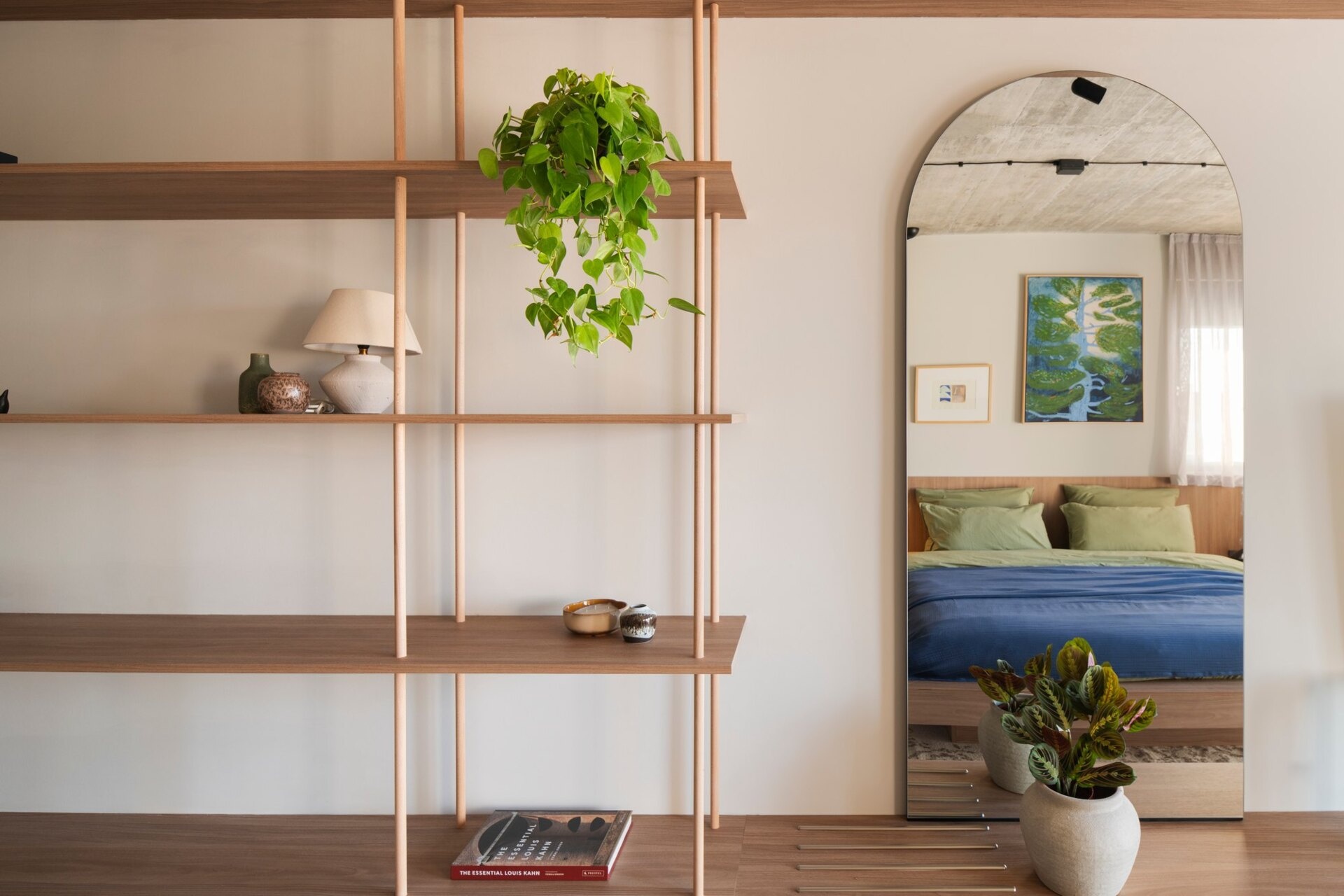 Take a look at a guest bedroom in Arc House, Croatia, featuring sage-green wardrobes, a timber headboard, blue and green bedding, open display shelves, indoor plants and a full-length arched mirror.