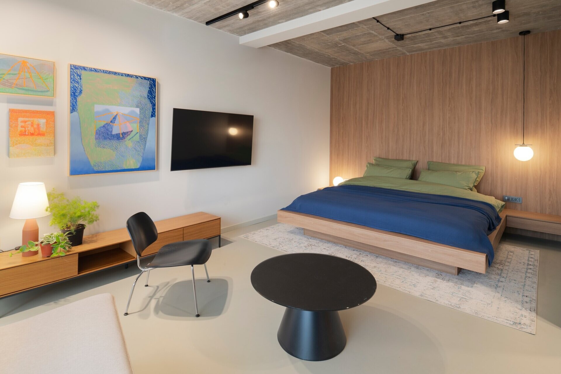 Discover a guest bedroom at Arc House, with a modern timber bed, black lounge chair, low wooden storage cabinet, colourful gallery wall and contemporary bedroom furniture in a Croatian villa.