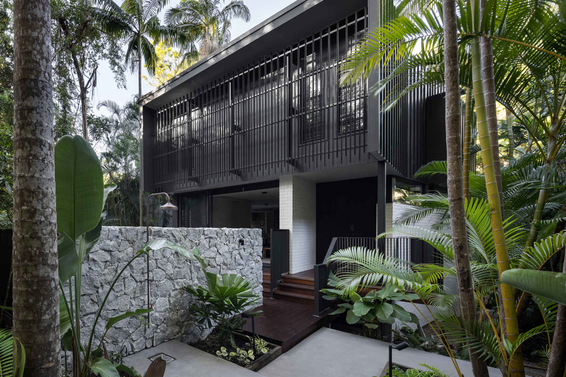 Explore the architecture of Raintree in Noosa Heads, Australia, designed by Void Building Design. Black vertical screens, natural stone walls, timber walkways, and lush rainforest vegetation define this contemporary coastal home.