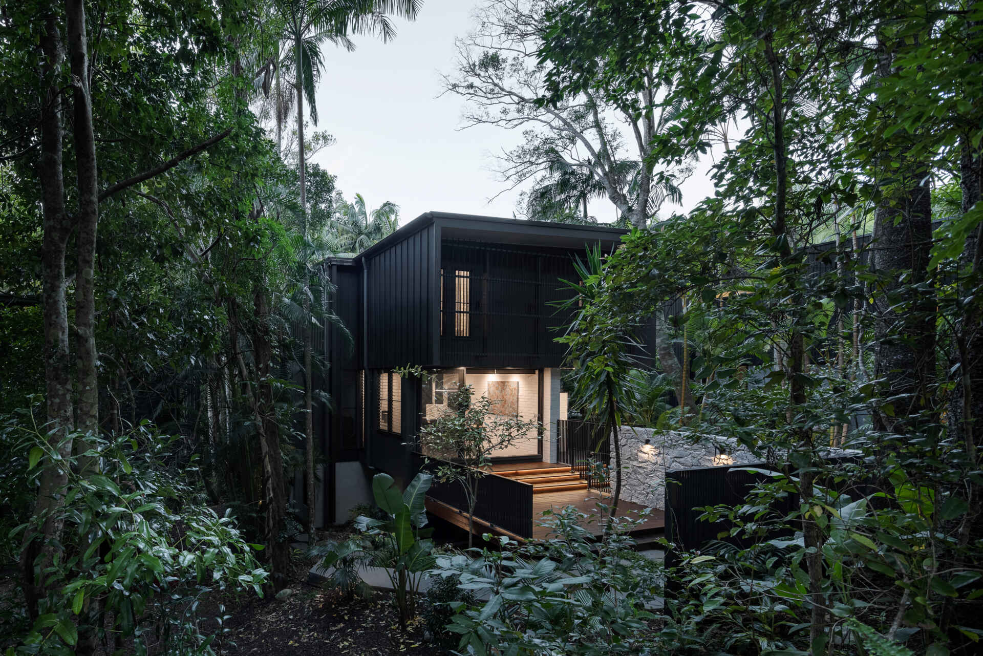 Explore the architecture of Raintree in Noosa Heads, Australia, designed by Void Building Design. Black vertical screens, natural stone walls, timber walkways, and lush rainforest vegetation define this contemporary coastal home.