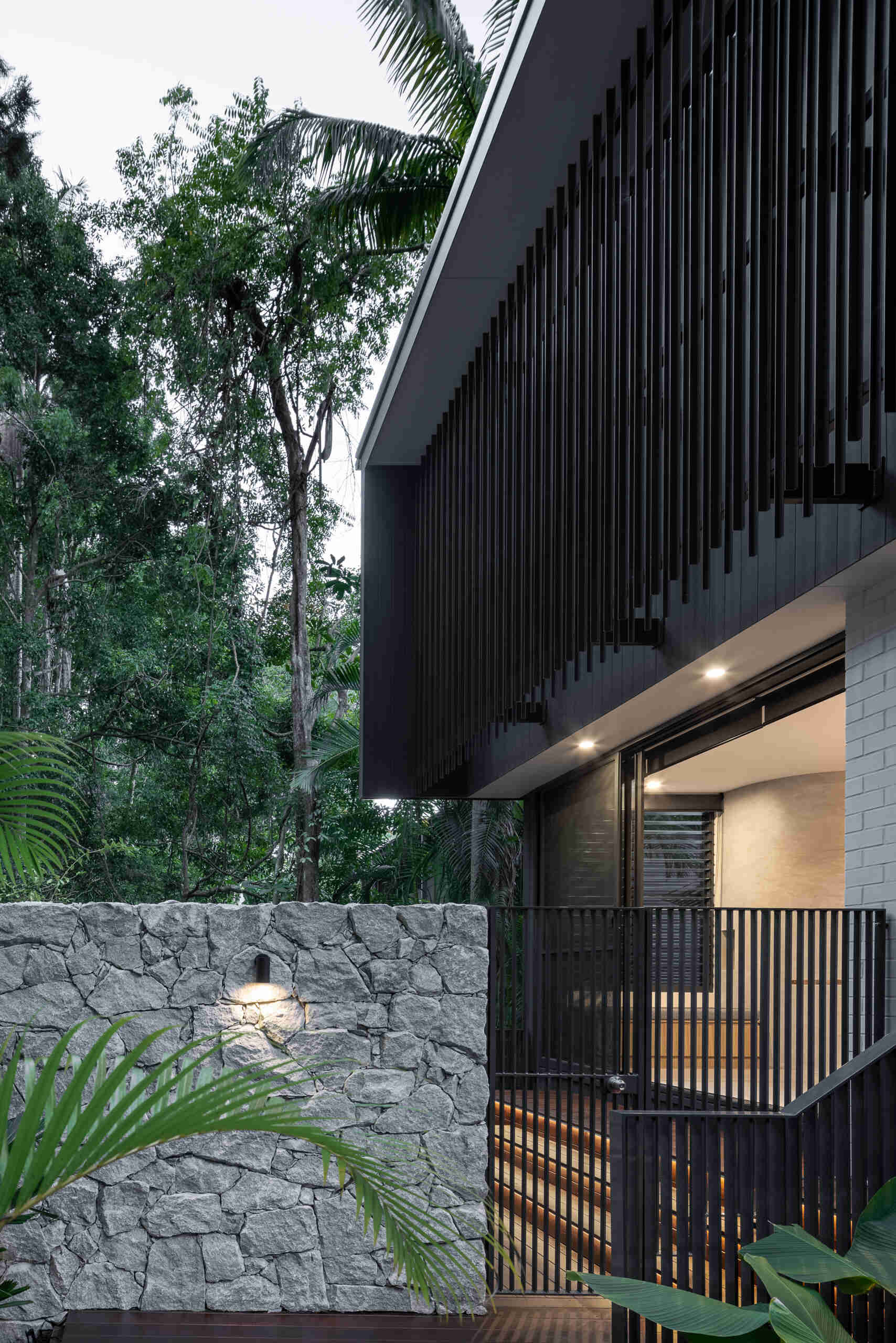 Explore the architecture of Raintree in Noosa Heads, Australia, designed by Void Building Design. Black vertical screens, natural stone walls, timber walkways, and lush rainforest vegetation define this contemporary coastal home.
