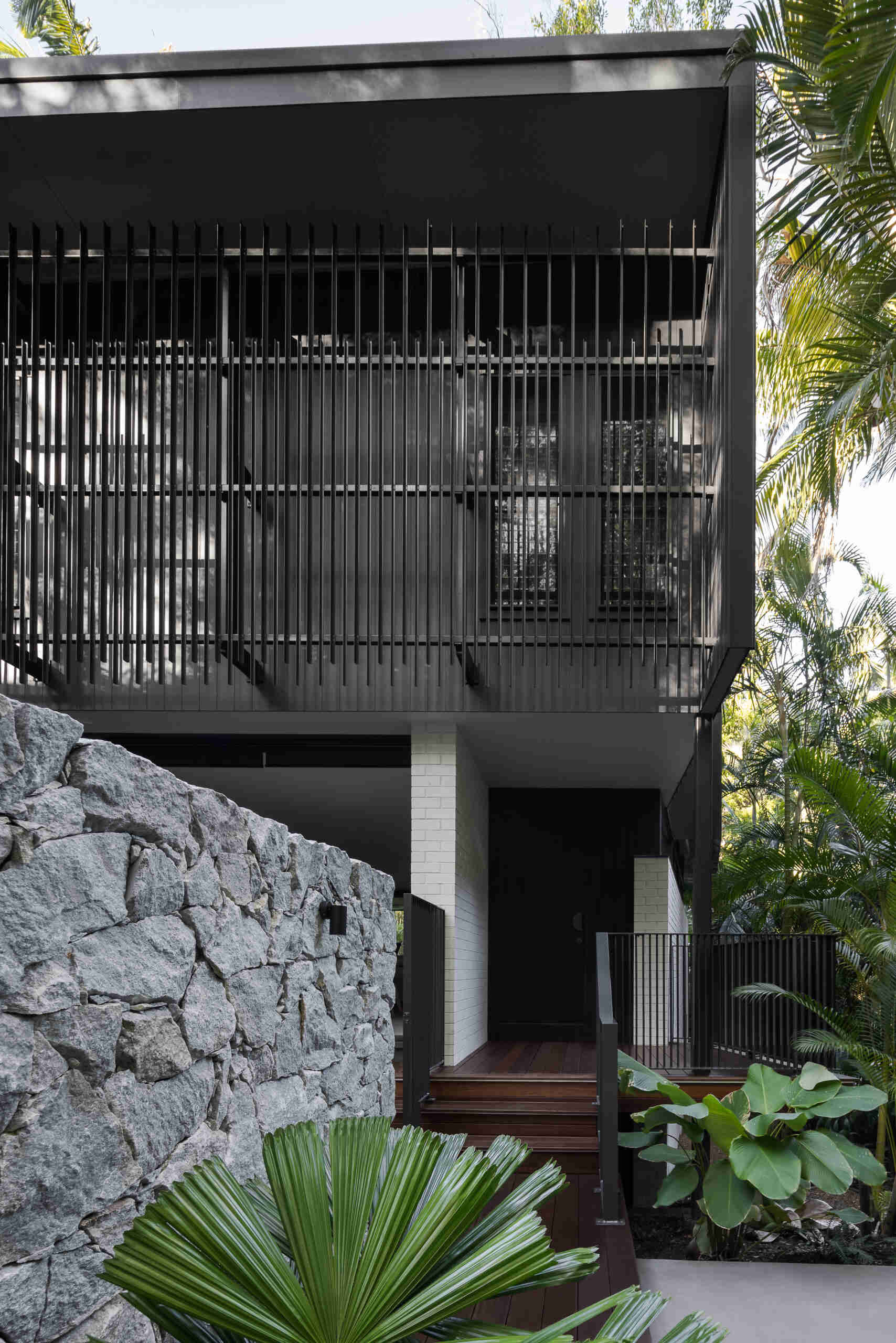 Explore the architecture of Raintree in Noosa Heads, Australia, designed by Void Building Design. Black vertical screens, natural stone walls, timber walkways, and lush rainforest vegetation define this contemporary coastal home.