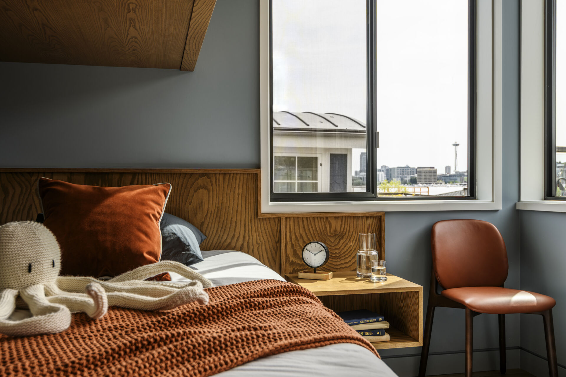 Featuring custom wood bunk beds, stainless steel railings, nautical wallpaper on the ceiling, a built-in desk, and warm orange accents, this compact bedroom combines playful design with practical storage.
