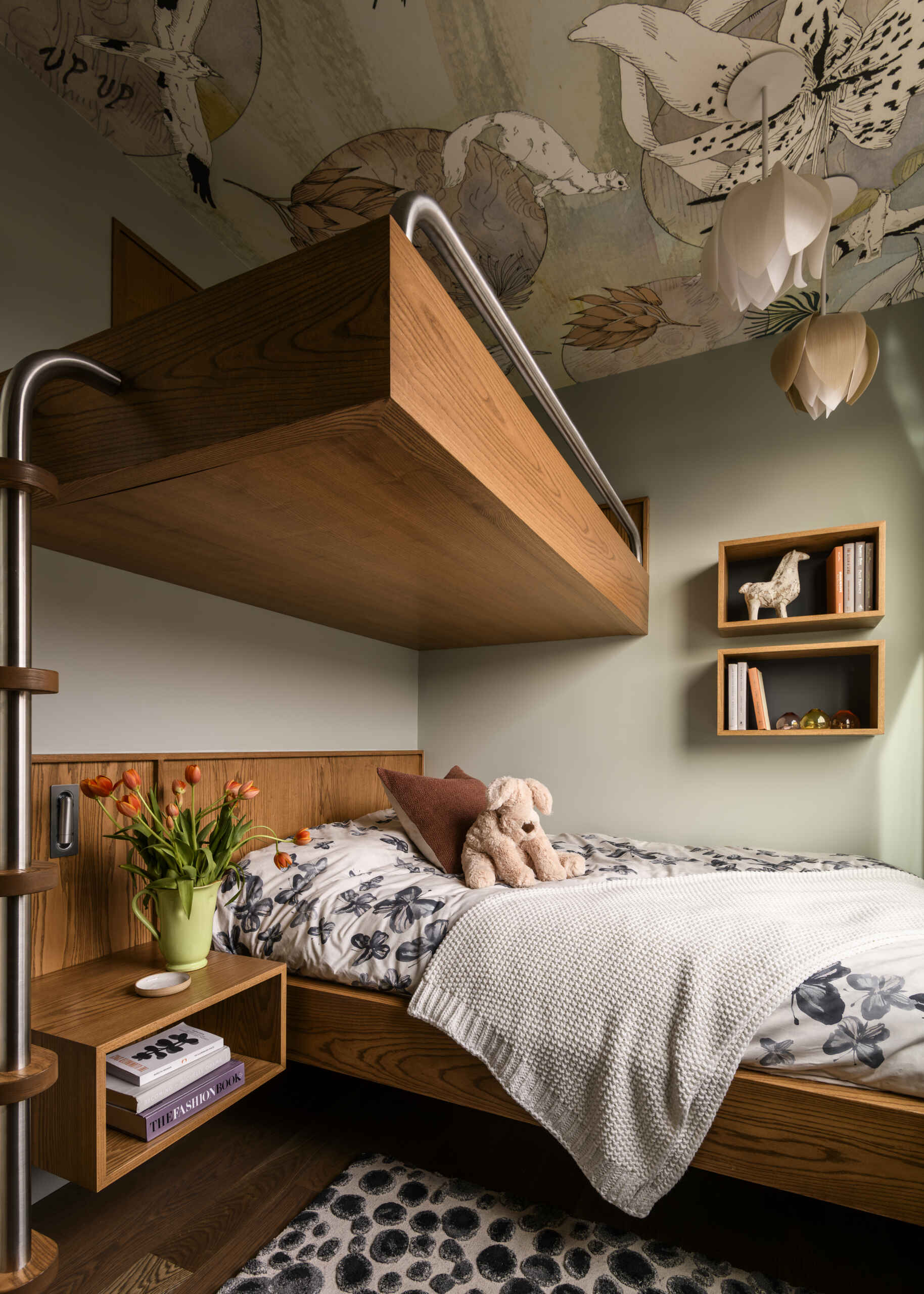 Custom wood bunk beds, botanical ceiling wallpaper, floral bedding, sculptural pendant lights, and a built-in desk create a cozy and practical kids' bedroom.