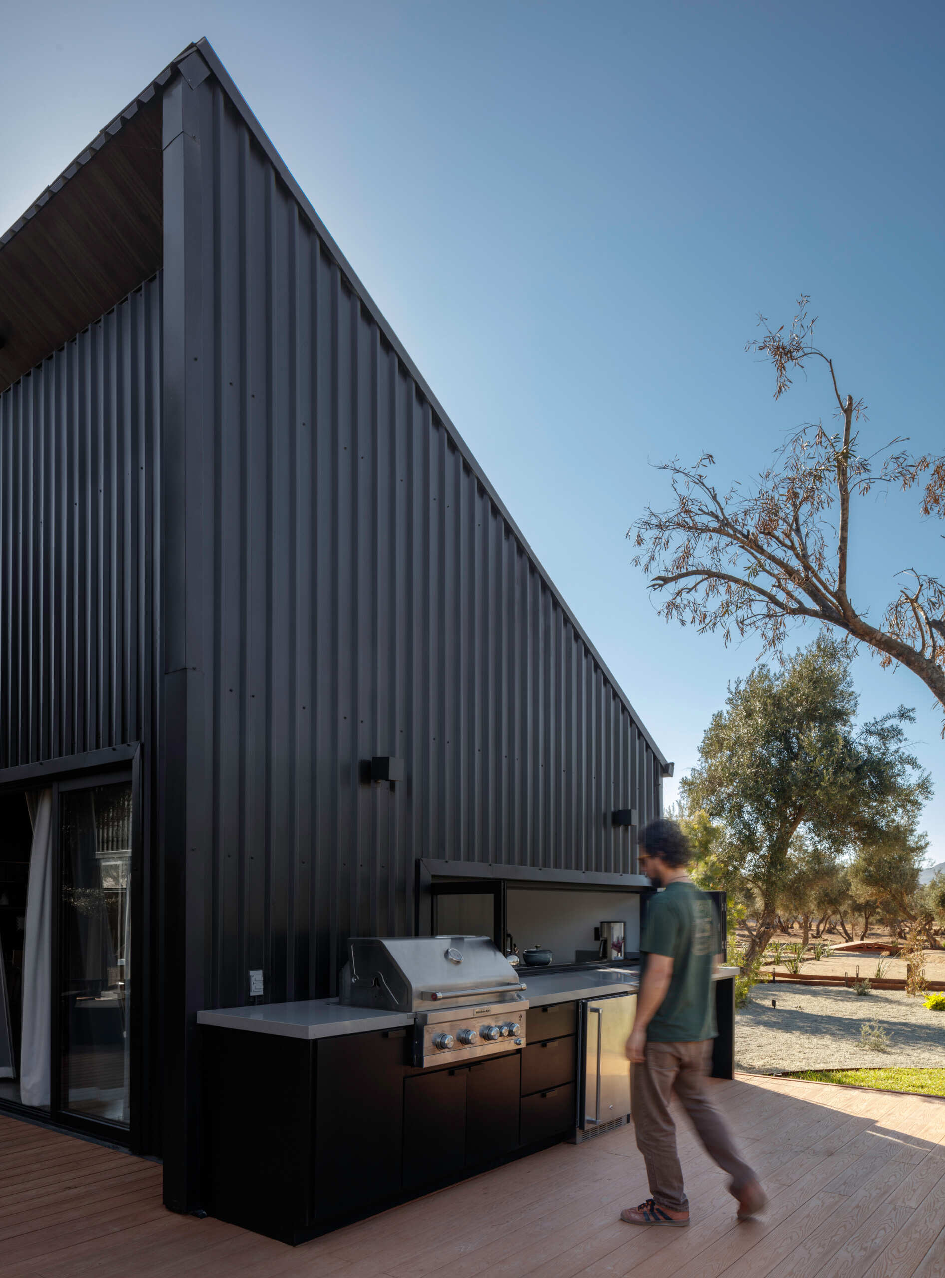 Discover the outdoor kitchen at Serentha Cabin by ORTO STUDIO in Baja California, Mexico. A built-in stainless steel barbecue, black cabinets, spacious countertops, and a pass-through kitchen window make this modern cabin ideal for outdoor cooking and entertaining.