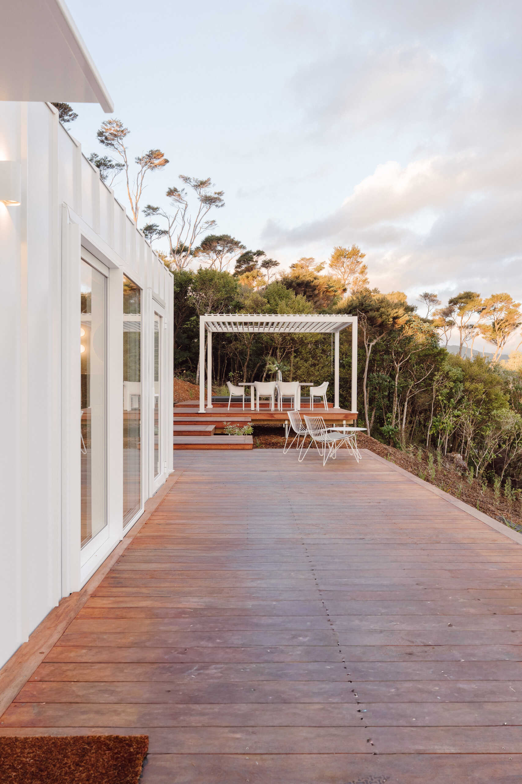 Explore the outdoor living spaces of a modern Coromandel cabin, featuring expansive timber decking, a sunken outdoor bathtub, covered dining pavilion, glamping tents and spectacular coastal views. Inspiration for small holiday homes and outdoor entertaining.
