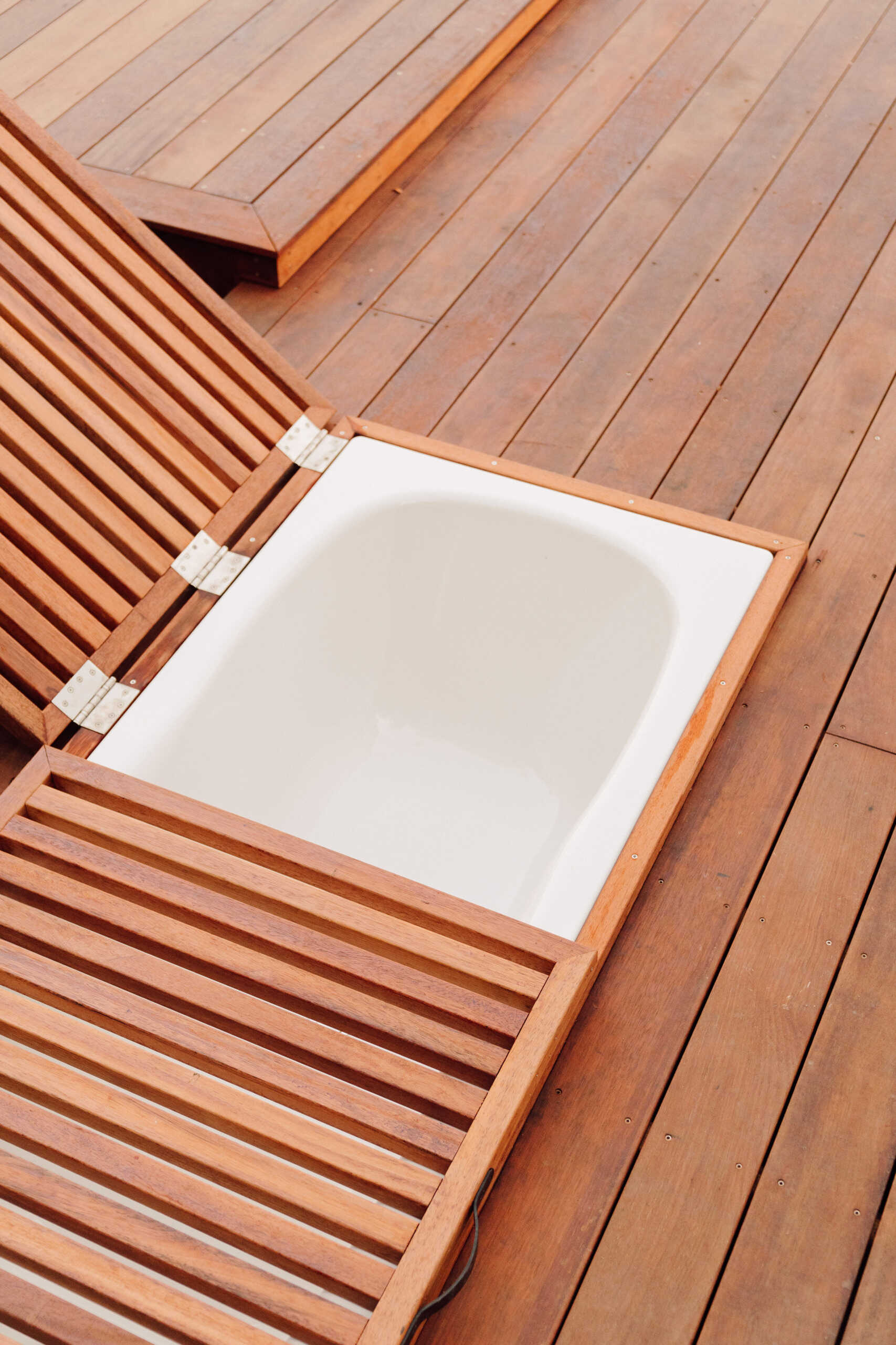 Explore the outdoor living spaces of a modern Coromandel cabin, featuring expansive timber decking, a sunken outdoor bathtub, covered dining pavilion, glamping tents and spectacular coastal views. Inspiration for small holiday homes and outdoor entertaining.