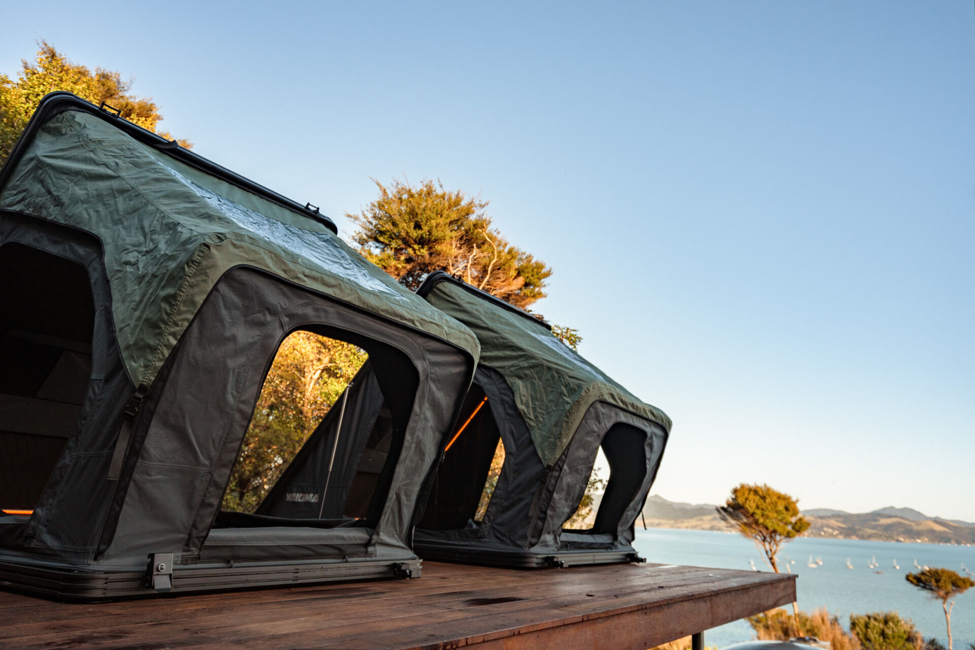 Explore the outdoor living spaces of a modern Coromandel cabin, featuring expansive timber decking, a sunken outdoor bathtub, covered dining pavilion, glamping tents and spectacular coastal views. Inspiration for small holiday homes and outdoor entertaining.