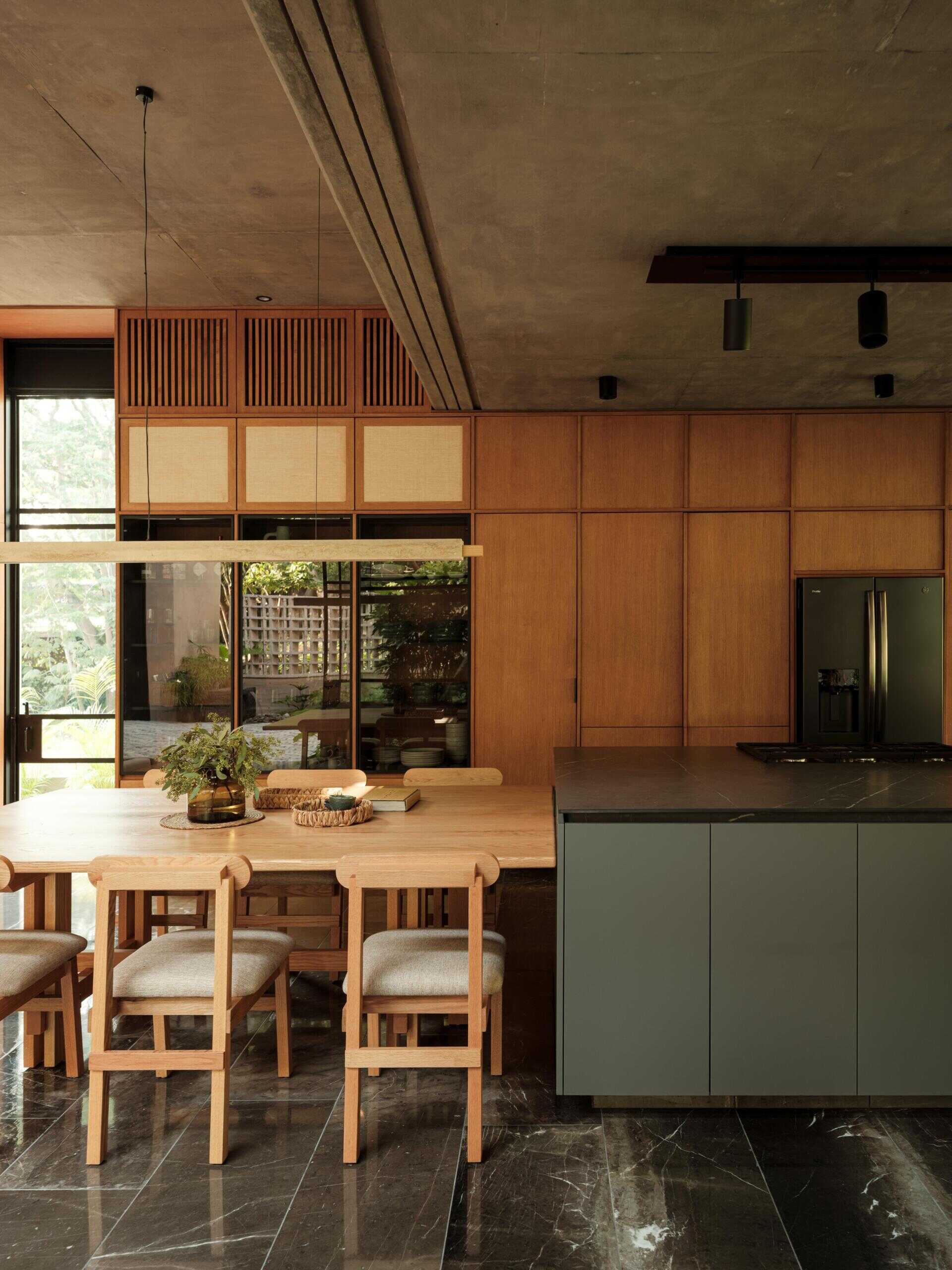 Explore a modern dining room and kitchen in Casa Akina, Mexico, featuring a solid wood dining table, custom timber cabinetry, a dark stone kitchen island, minimalist lighting, and large windows overlooking tropical greenery.