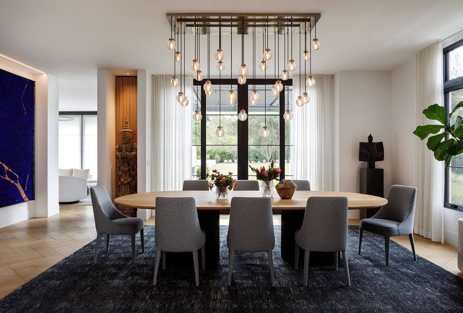 Explore the Atherton Residence formal dining room by Paulina Carcach Studio, featuring a custom two-tone dining table, grey upholstered chairs, cascading glass pendant lights and a collection of large-scale art and sculpture.