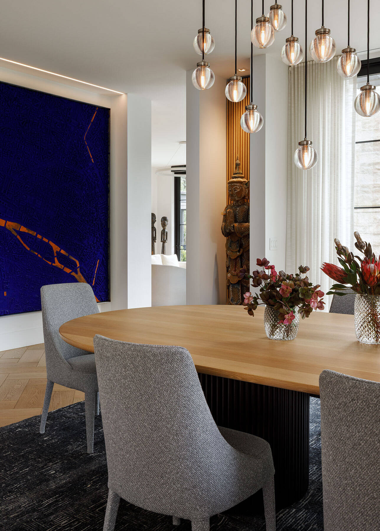 Explore the Atherton Residence formal dining room by Paulina Carcach Studio, featuring a custom two-tone dining table, grey upholstered chairs, cascading glass pendant lights and a collection of large-scale art and sculpture.
