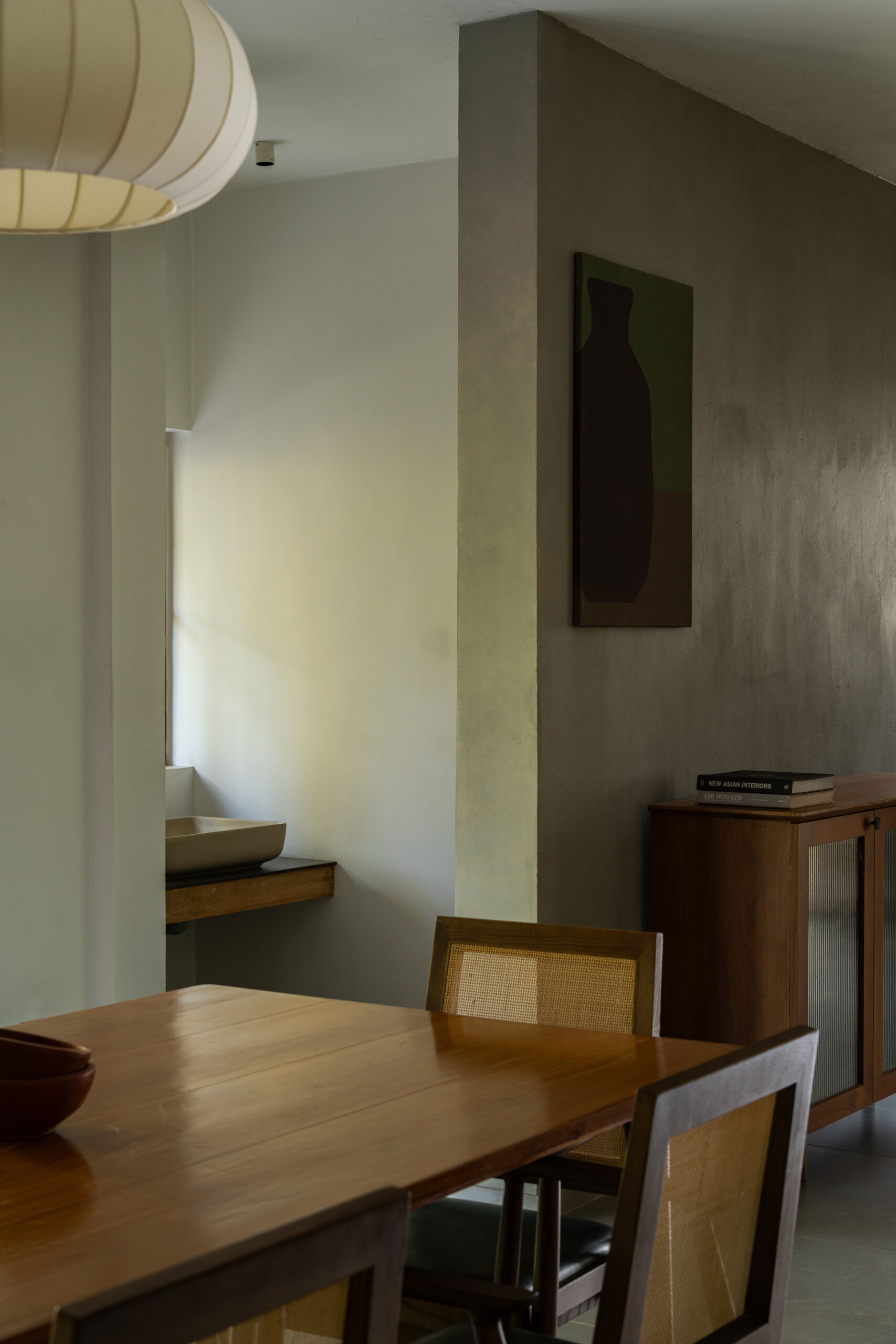 A modern dining room in Kerala features a large wooden table, six cane-back dining chairs, a white pendant light, and garden-facing windows.