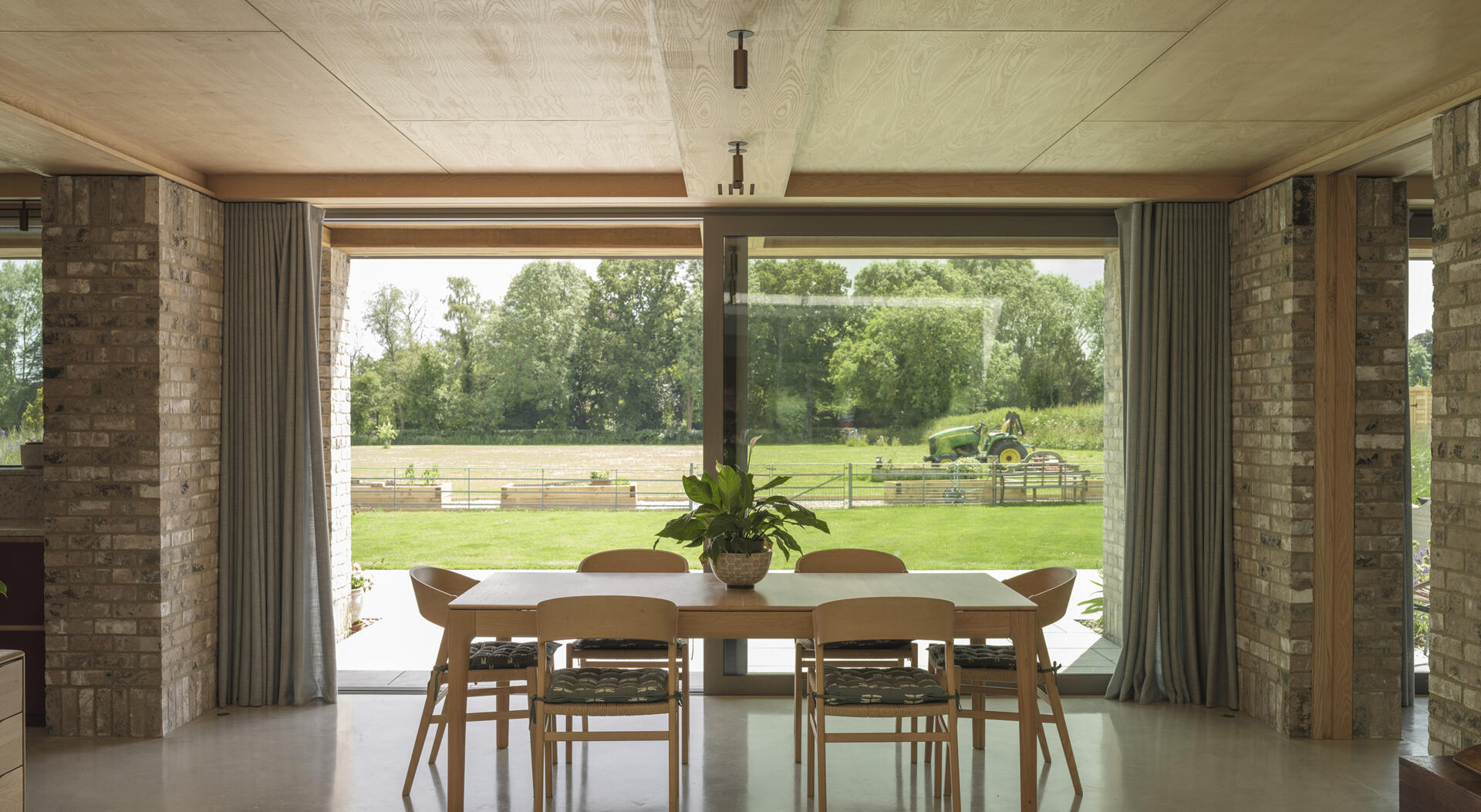 Exposed brick columns, pale wood ceilings, large sliding glass doors, and polished concrete floors bring natural textures into this contemporary open-plan home.