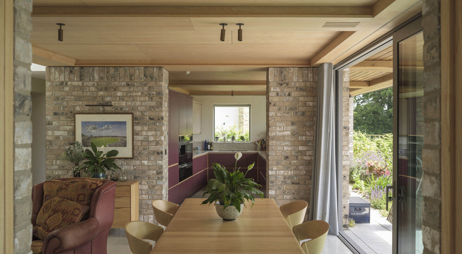 Exposed brick columns, pale wood ceilings, large sliding glass doors, and polished concrete floors bring natural textures into this contemporary open-plan home.