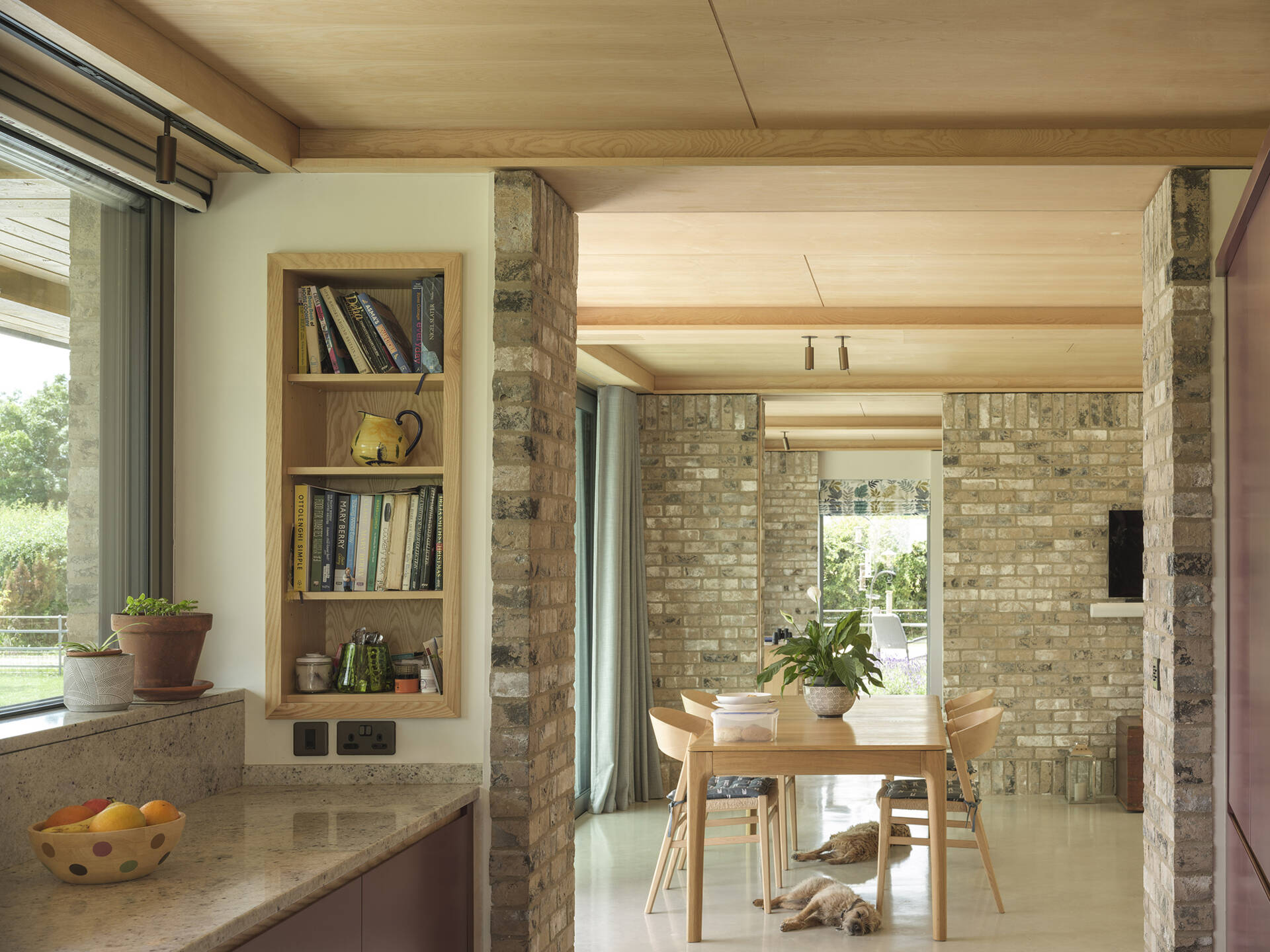 Exposed brick columns, pale wood ceilings, large sliding glass doors, and polished concrete floors bring natural textures into this contemporary open-plan home.