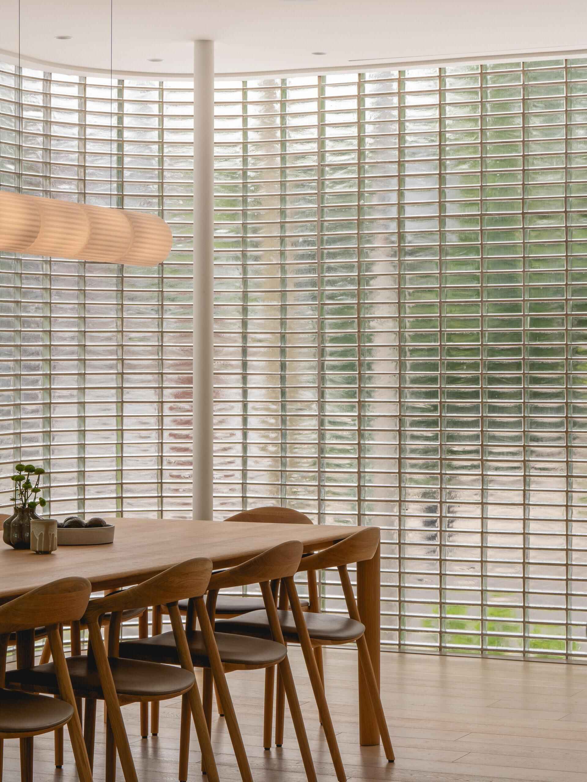 Discover the curved glass-brick dining room at The Lens, a contemporary Montreal home by MU Architecture. A warm timber dining table, sculptural pendant lighting, and translucent glass walls create a beautiful minimalist interior.