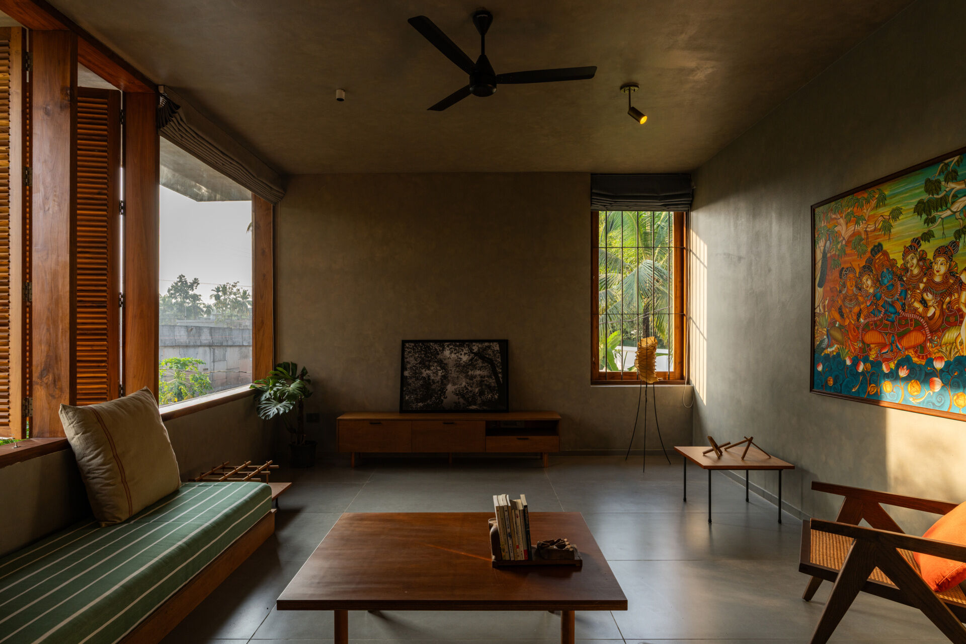 An upper-floor entertainment room with wooden shutters, a green daybed, a built-in desk, and treetop views shows how contemporary design can embrace its natural surroundings.