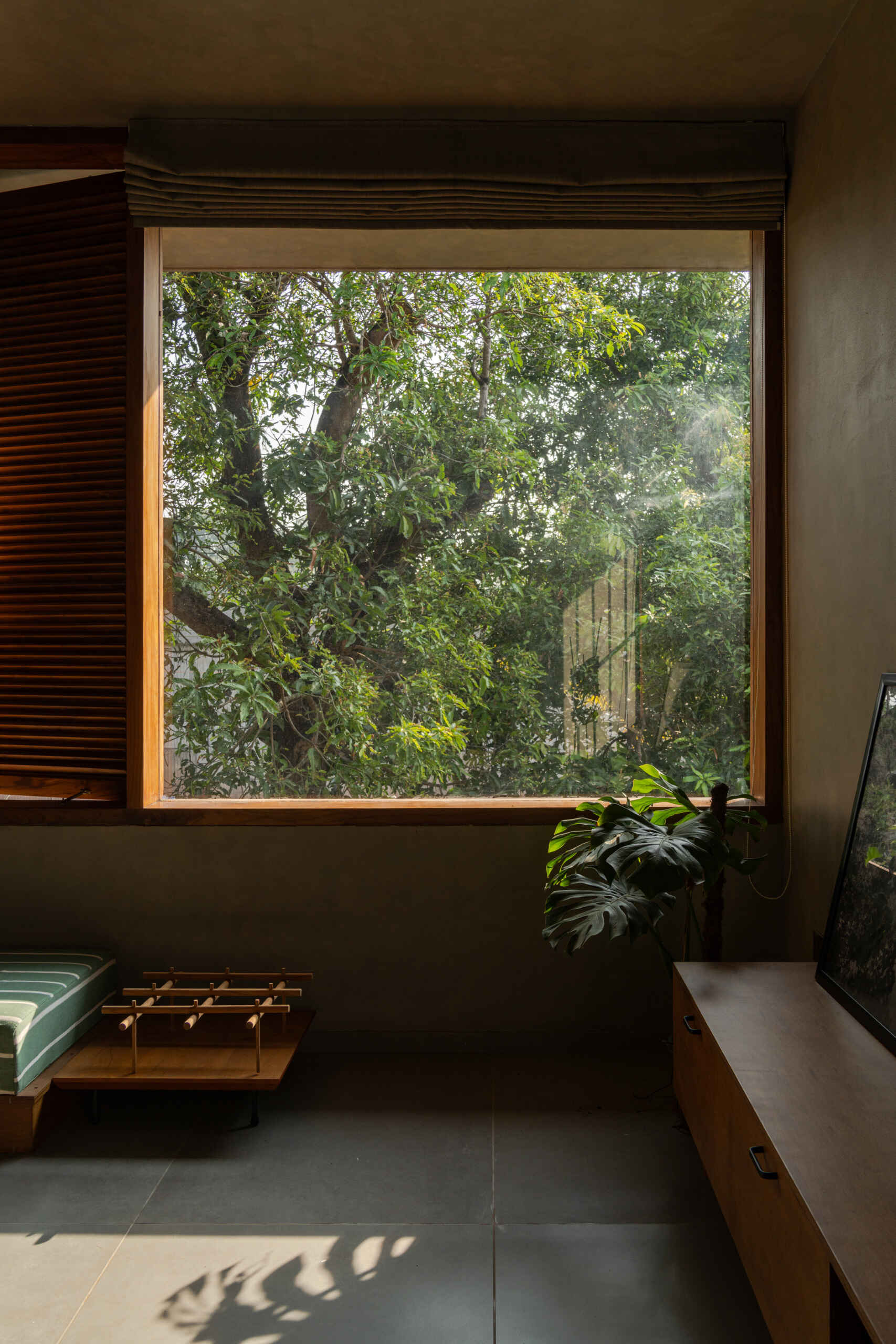 An upper-floor entertainment room with wooden shutters, a green daybed, a built-in desk, and treetop views shows how contemporary design can embrace its natural surroundings.