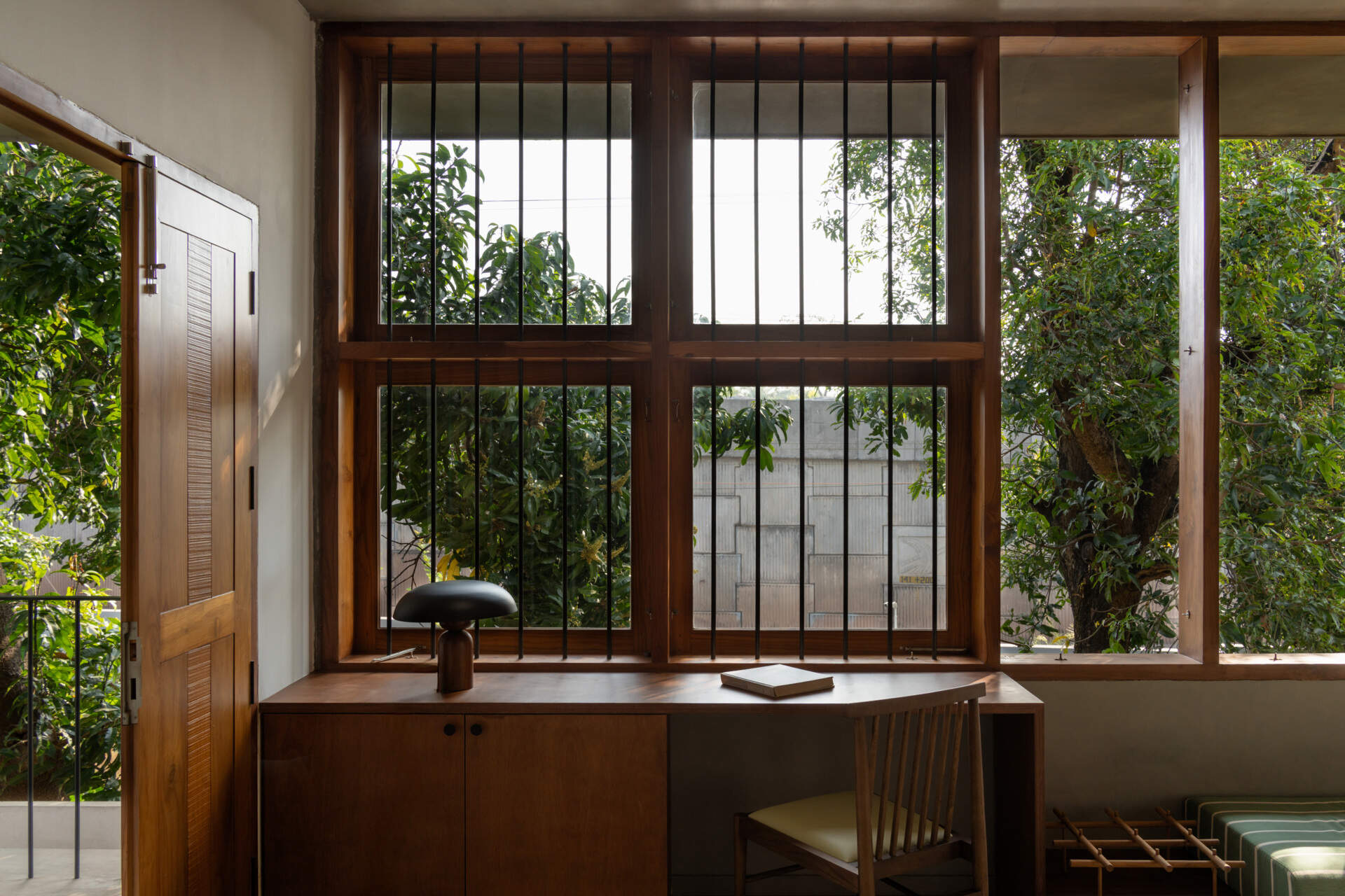 An upper-floor entertainment room with wooden shutters, a green daybed, a built-in desk, and treetop views shows how contemporary design can embrace its natural surroundings.