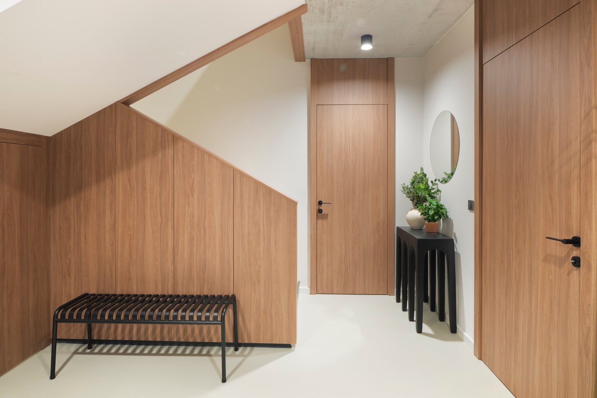 Step inside the modern entryway of Arc House in Croatia, featuring warm timber wall panelling, concealed under-stair storage, a black metal bench, sculptural console table and minimalist contemporary interior design.