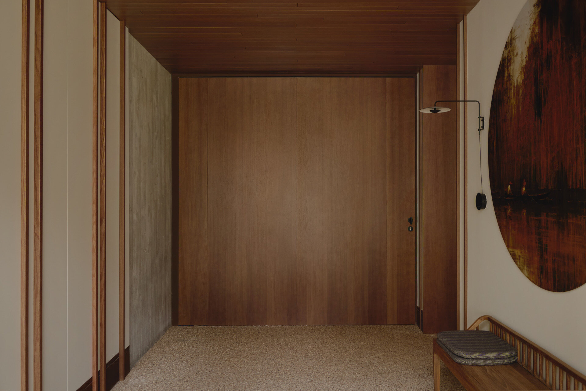 Step inside Casa Tossal and explore its modern entryway, featuring floating-style concrete garden steps, wood ceilings, large wooden doors, sculptural artwork, and a minimalist wooden bench.