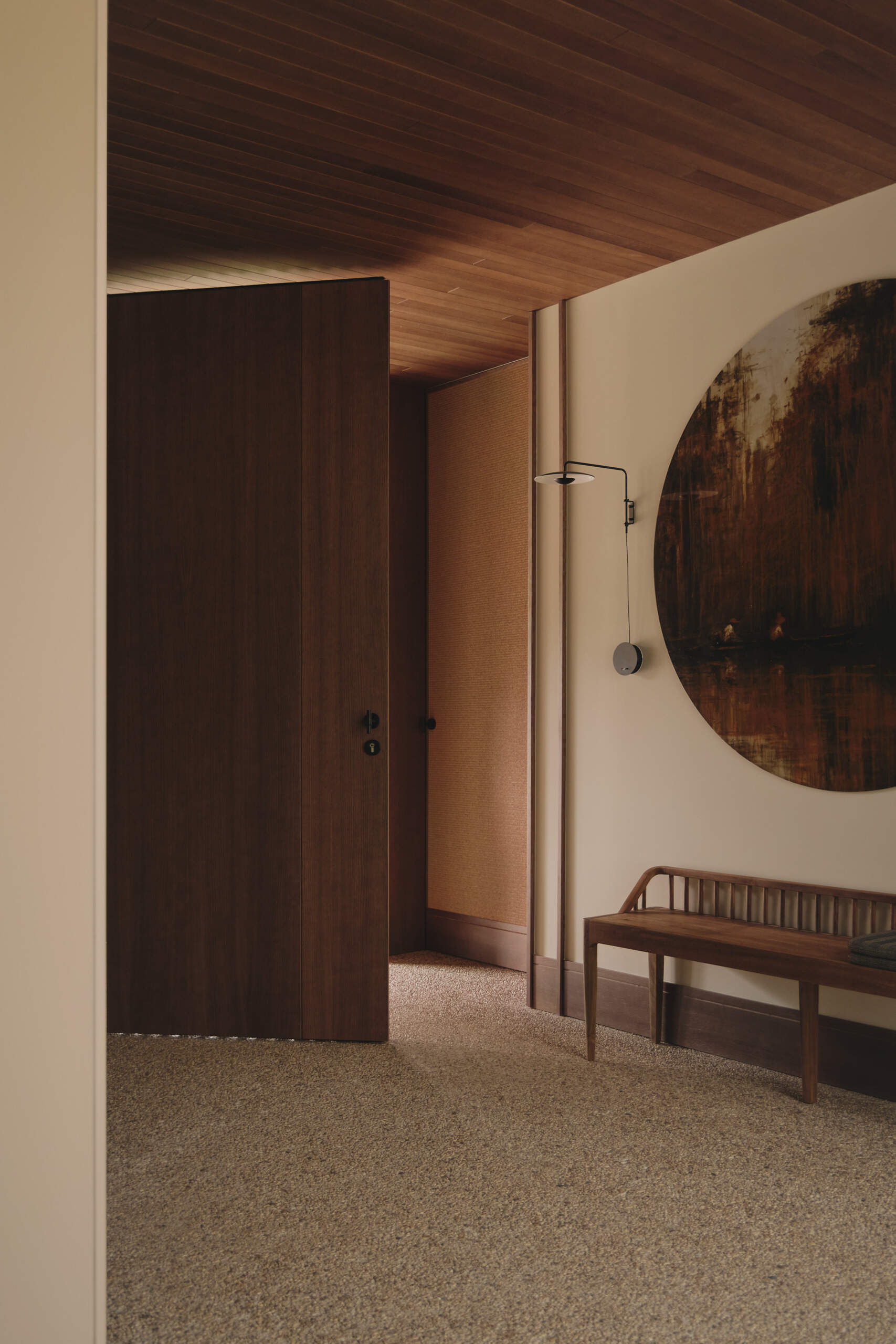 Step inside Casa Tossal and explore its modern entryway, featuring floating-style concrete garden steps, wood ceilings, large wooden doors, sculptural artwork, and a minimalist wooden bench.