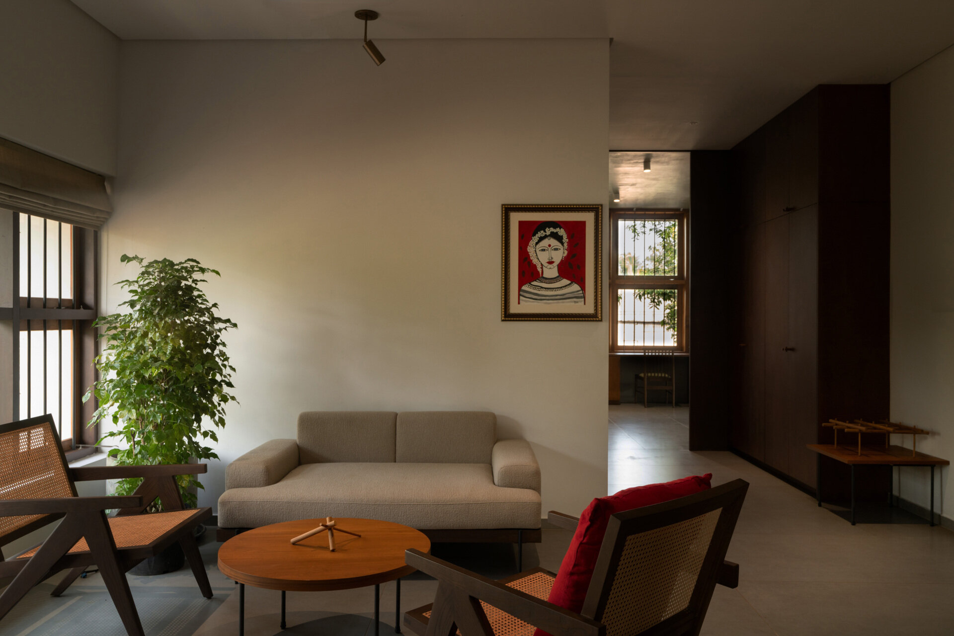 This upstairs family room features a neutral sofa, woven cane armchairs, warm timber furniture, indoor greenery, and small red accents for a relaxed contemporary interior.