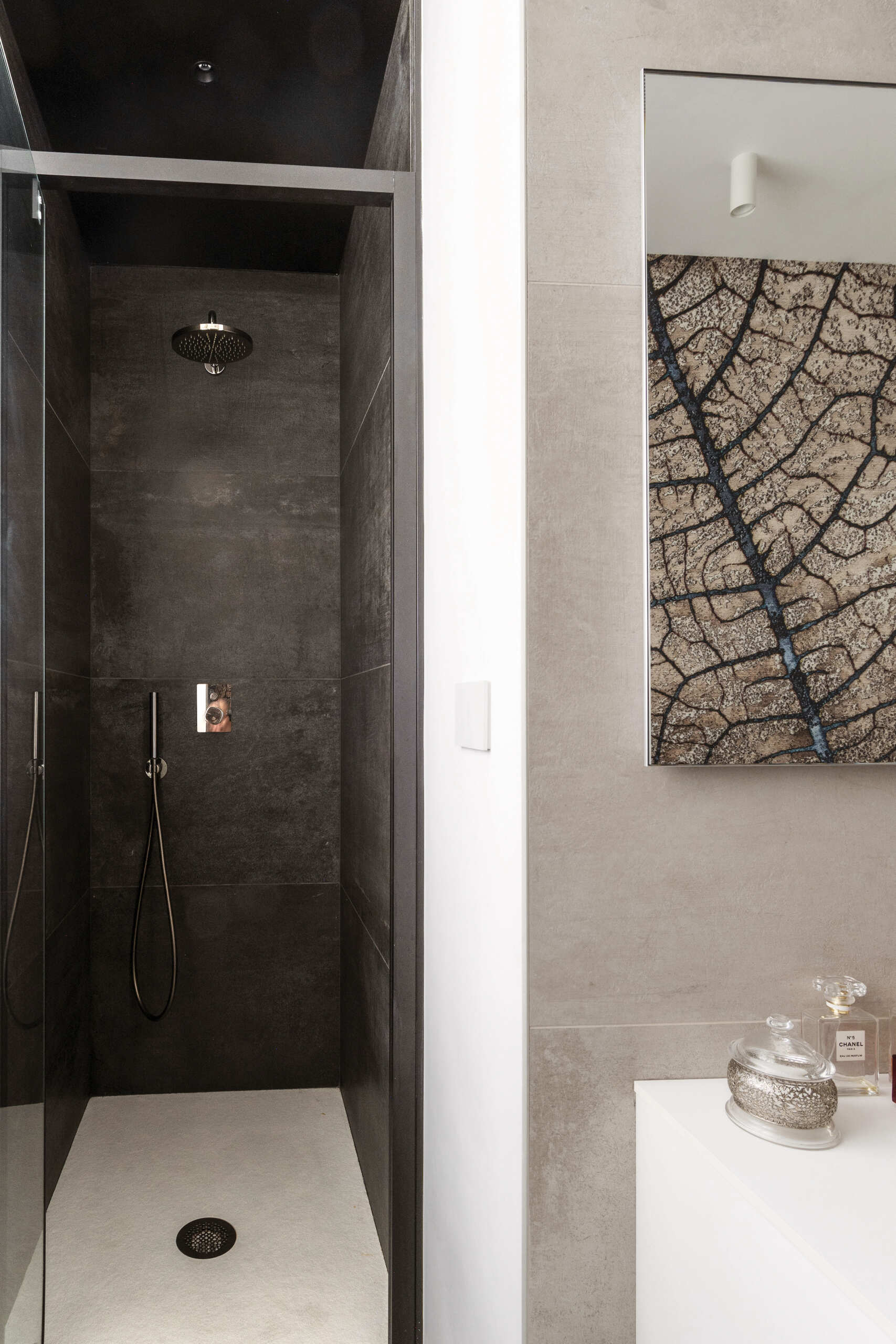 A hidden guest bathroom features dramatic tree-pattern wallpaper, a floating vanity, a large mirror, and a dark tiled shower, accessed from a textured hallway.