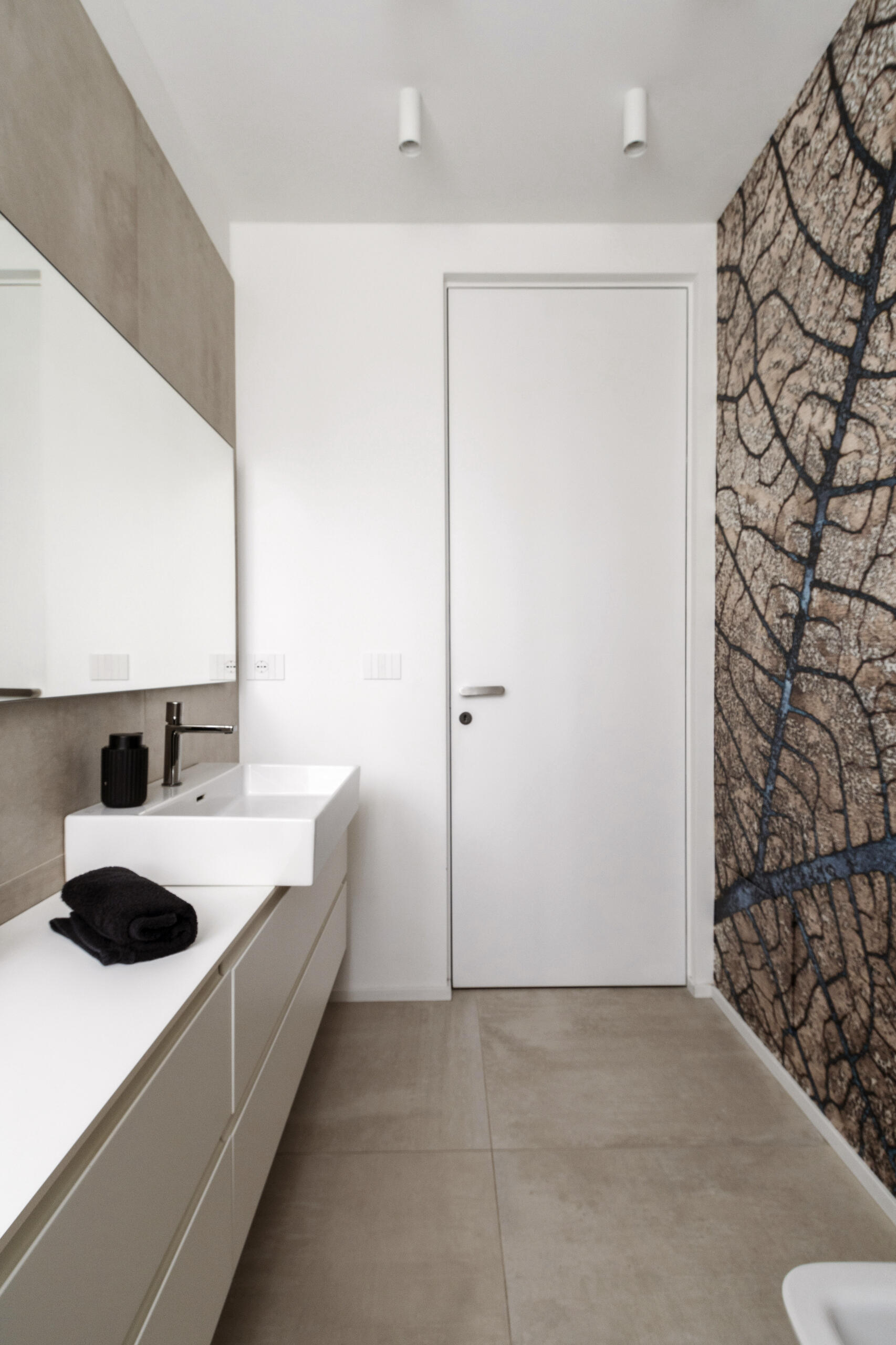 A hidden guest bathroom features dramatic tree-pattern wallpaper, a floating vanity, a large mirror, and a dark tiled shower, accessed from a textured hallway.