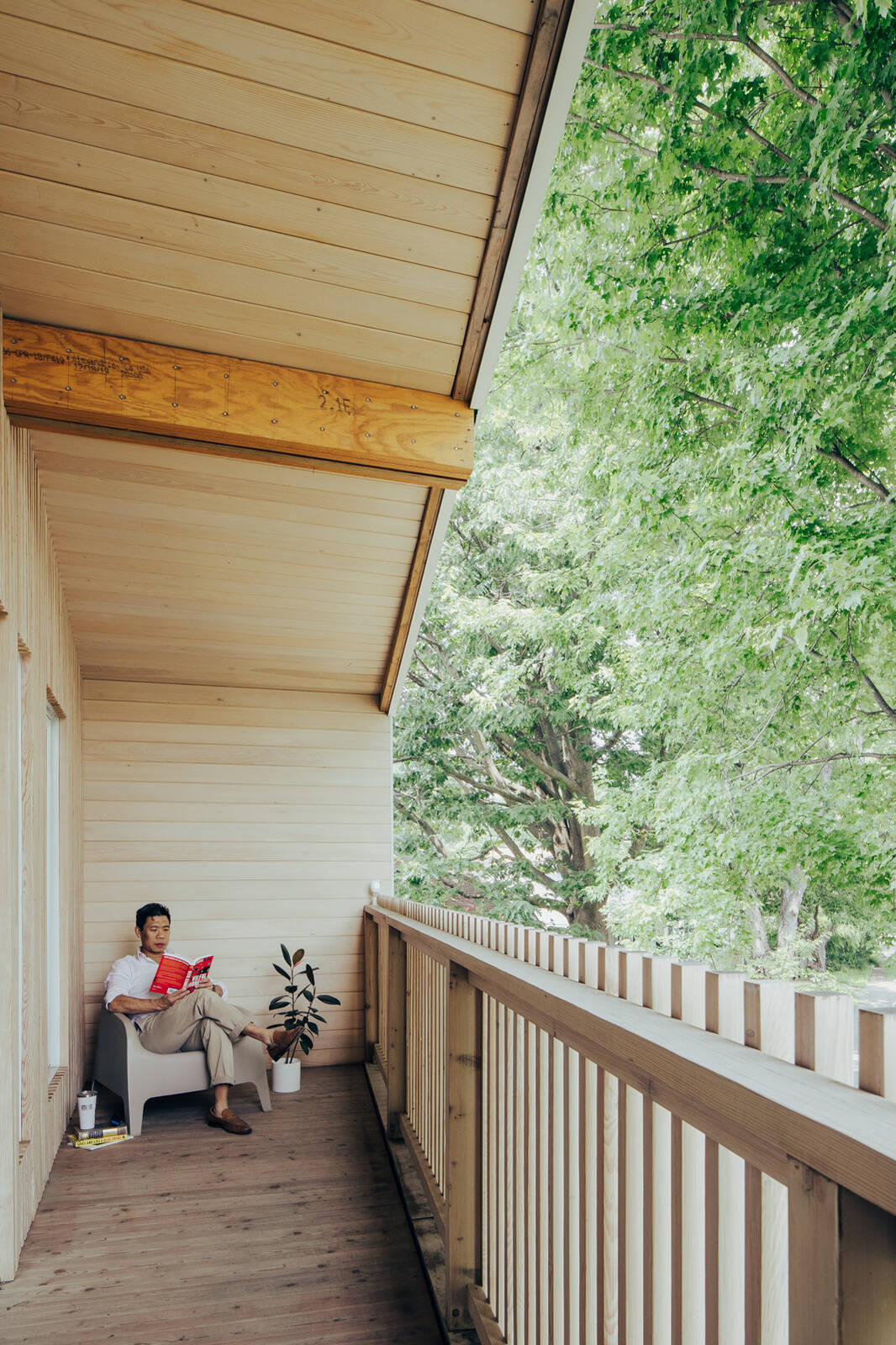 A covered second-floor balcony with timber decking, a wood-lined ceiling, and vertical railings overlooks a mature maple tree at this contemporary Ottawa home.