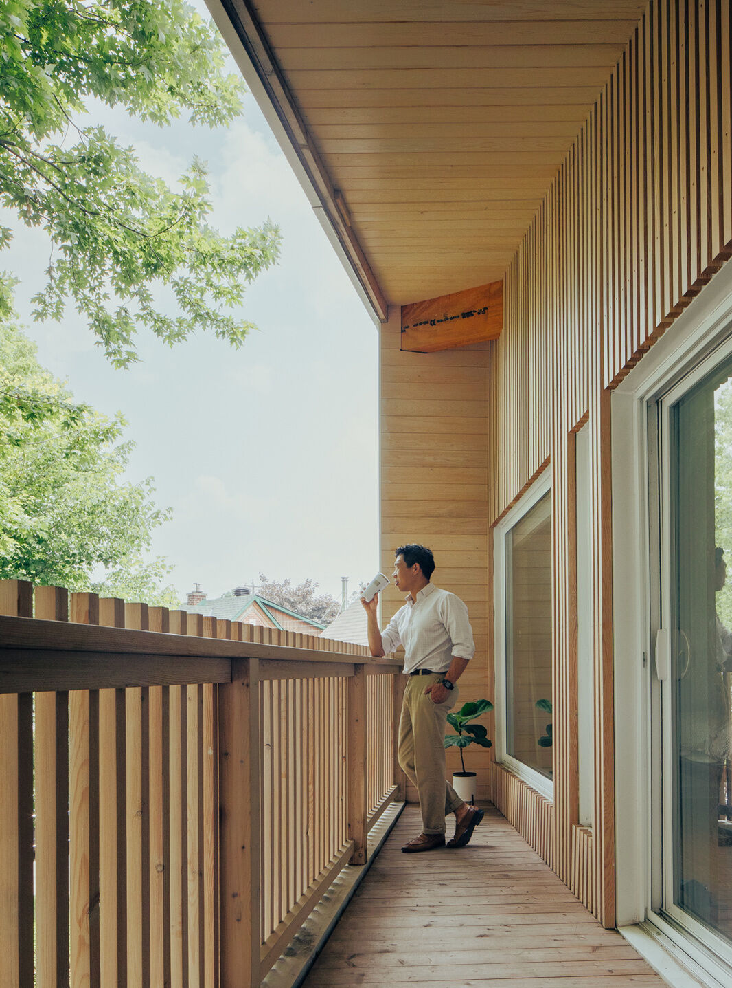 A covered second-floor balcony with timber decking, a wood-lined ceiling, and vertical railings overlooks a mature maple tree at this contemporary Ottawa home.