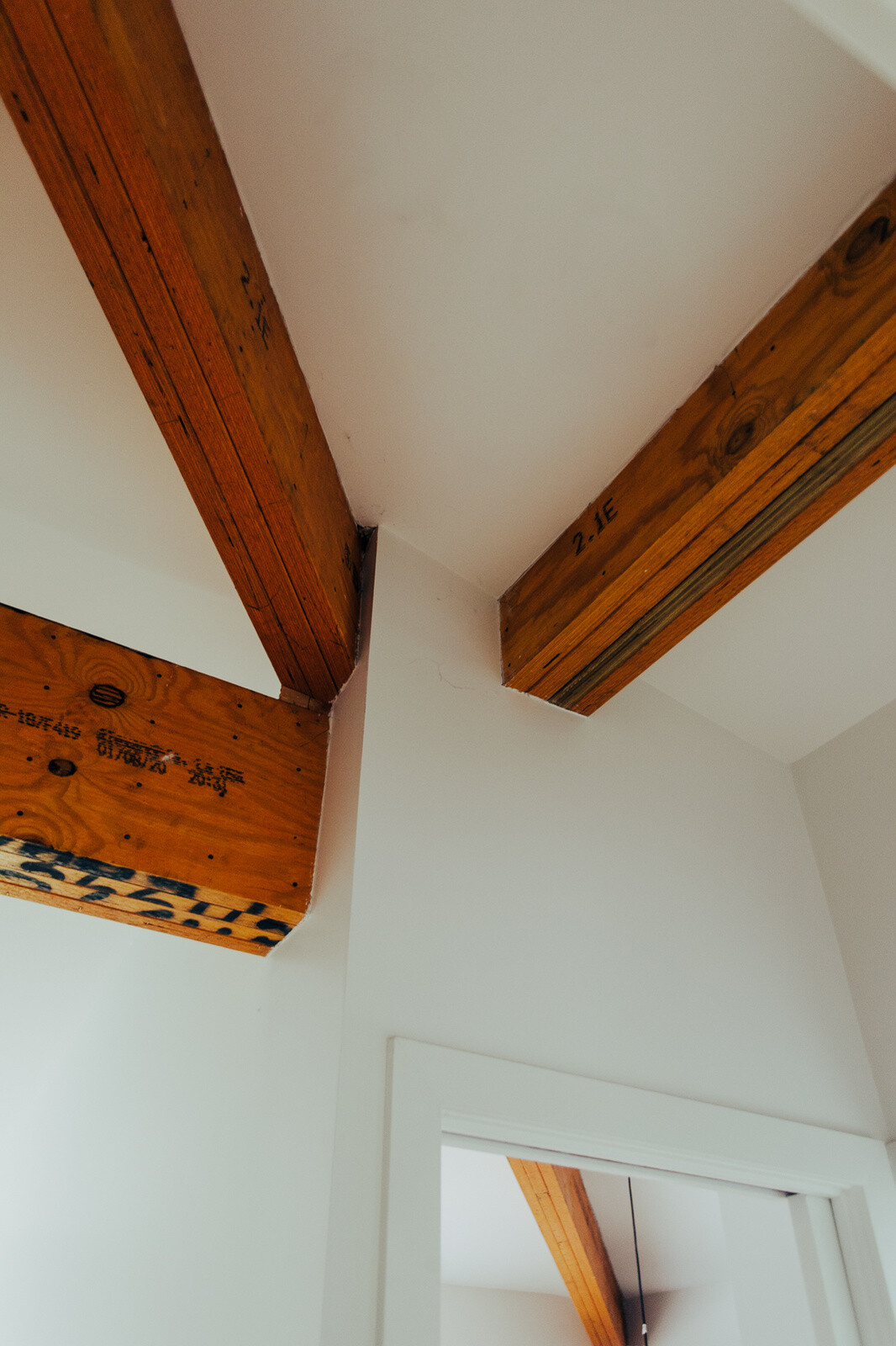 Exposed laminated veneer lumber beams bring warmth and architectural character to a contemporary white interior, with visible construction markings adding an industrial touch.