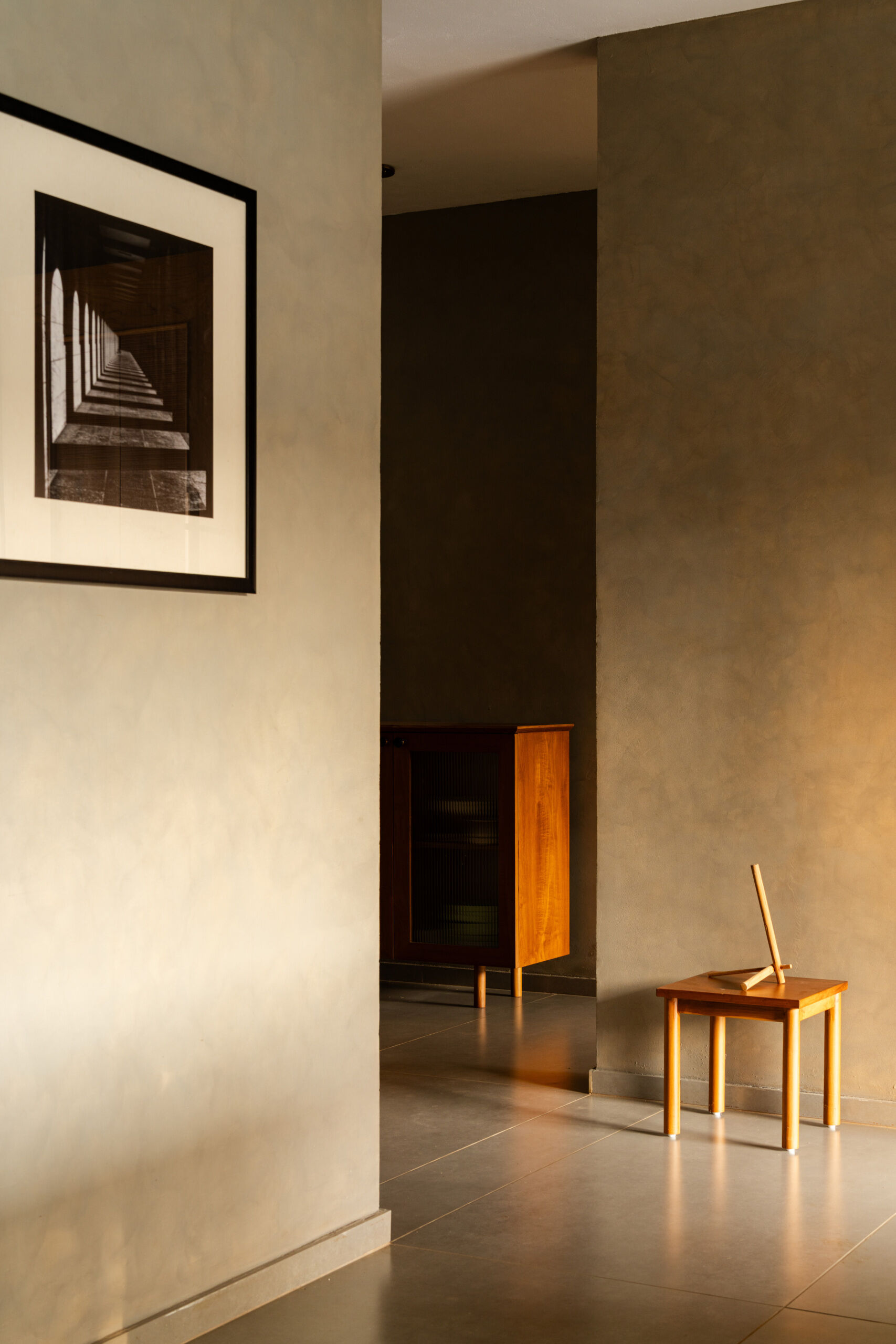 A minimalist foyer with grey walls, timber furniture, framed photography, and warm natural light welcomes visitors into this contemporary Indian home.