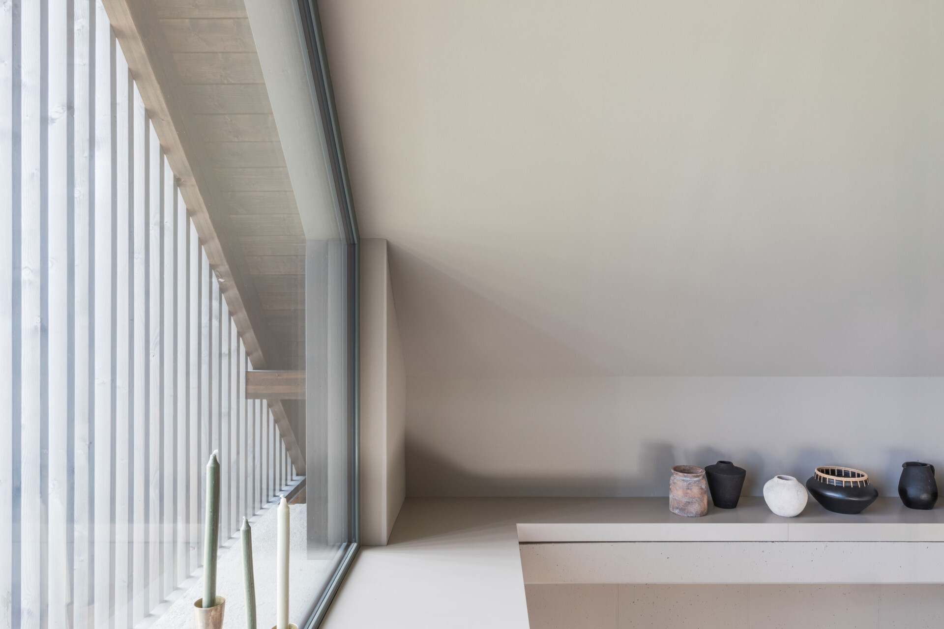 An upper-floor gallery lounge beneath a pitched roof features daybed seating, a record collection, bookshelves, and a large triangular window with timber screening.