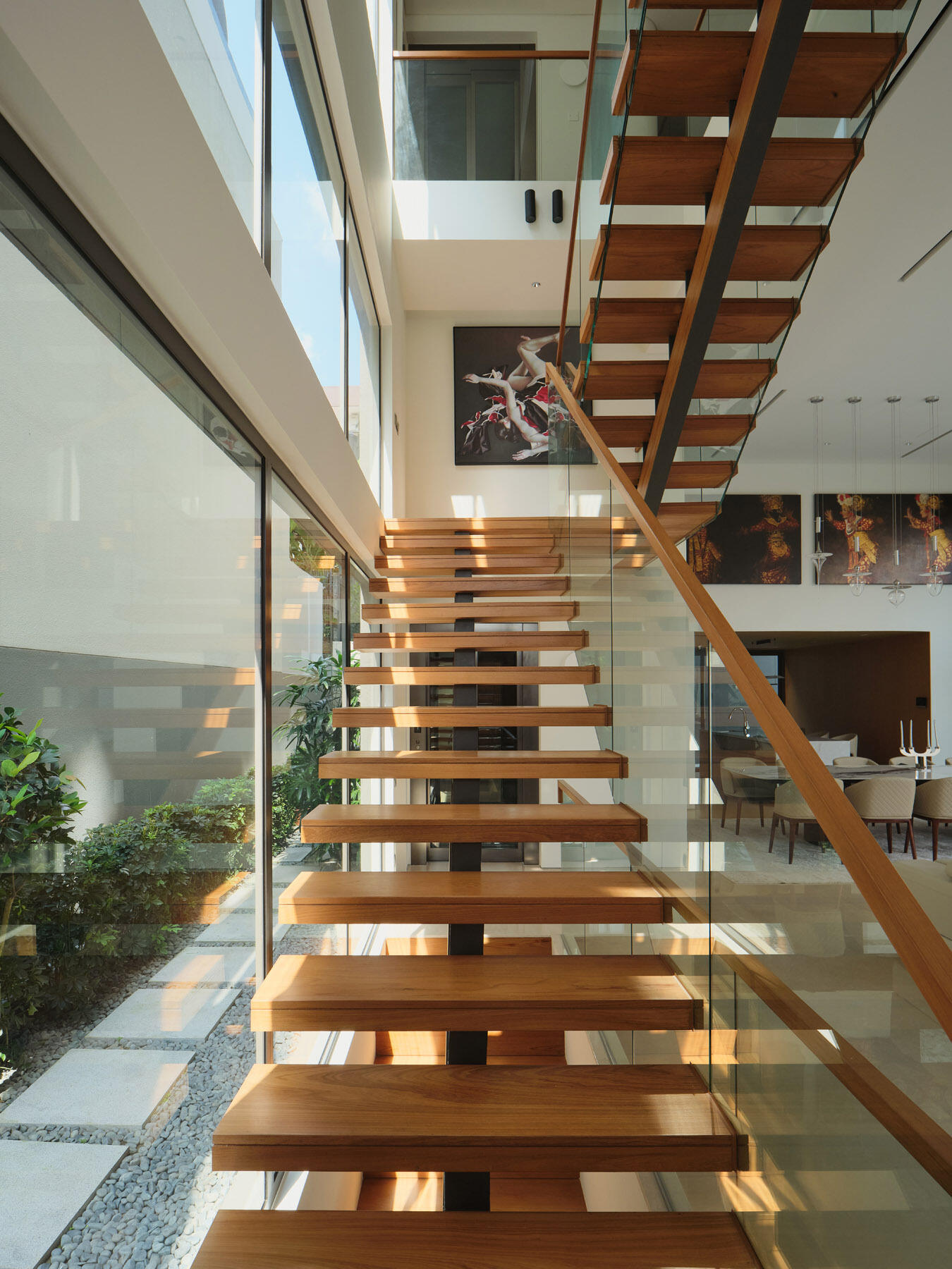 Explore the floating timber staircase in JS-House, featuring open wooden treads, glass balustrades, a central structural support, and skylights that bring daylight into the home.