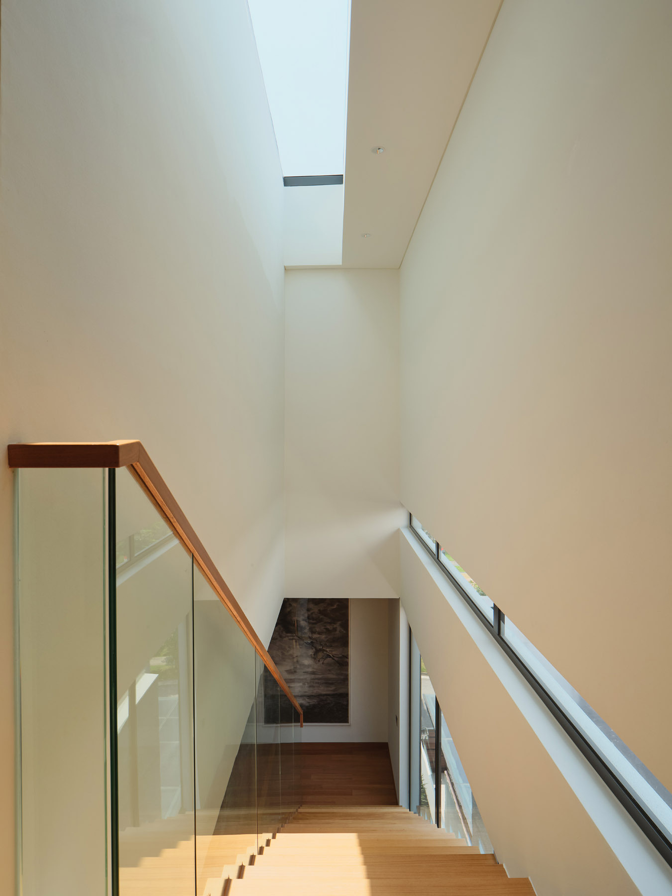 Explore the floating timber staircase in JS-House, featuring open wooden treads, glass balustrades, a central structural support, and skylights that bring daylight into the home.
