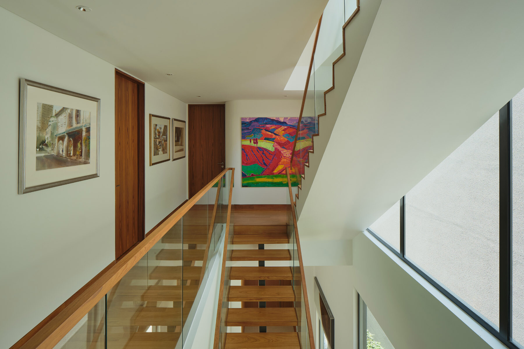 Explore the floating timber staircase in JS-House, featuring open wooden treads, glass balustrades, a central structural support, and skylights that bring daylight into the home.