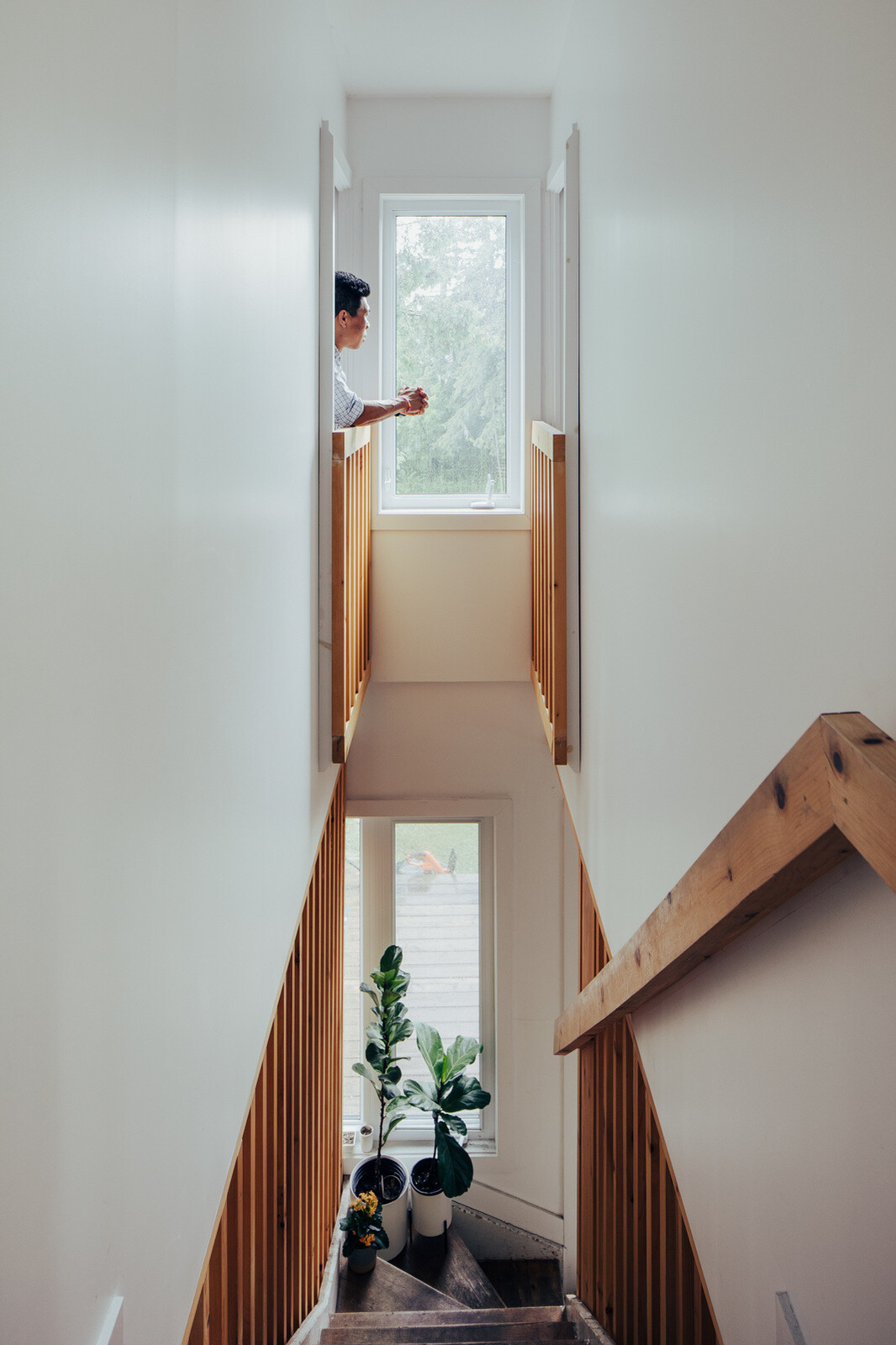 An original wooden staircase becomes an architectural feature in this renovated home, with weathered steps, new timber slat railings, tall white walls, and natural light.