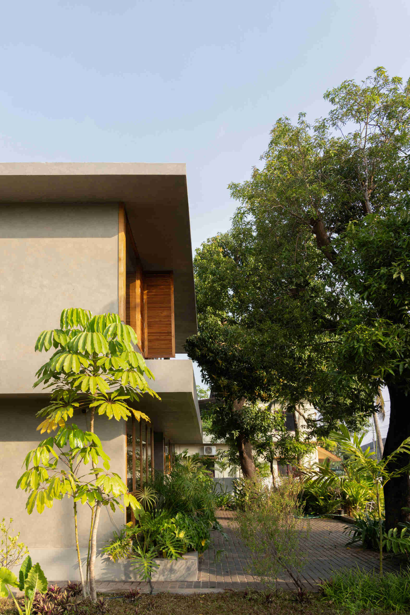 This contemporary house in Kerala features a minimalist façade, teak wood windows, shaded balconies, and two mature mango trees that provide natural privacy.