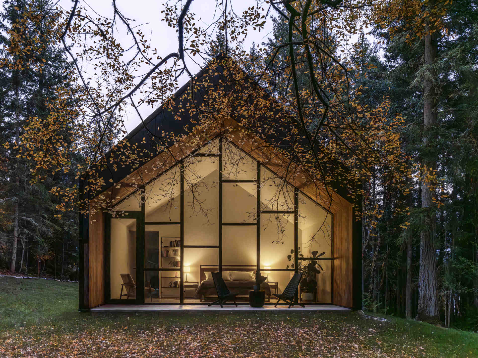 This modern gabled house on Vashon Island features black standing-seam metal, recessed timber walls, floor-to-ceiling glass, and a narrow footprint designed to preserve the surrounding forest.