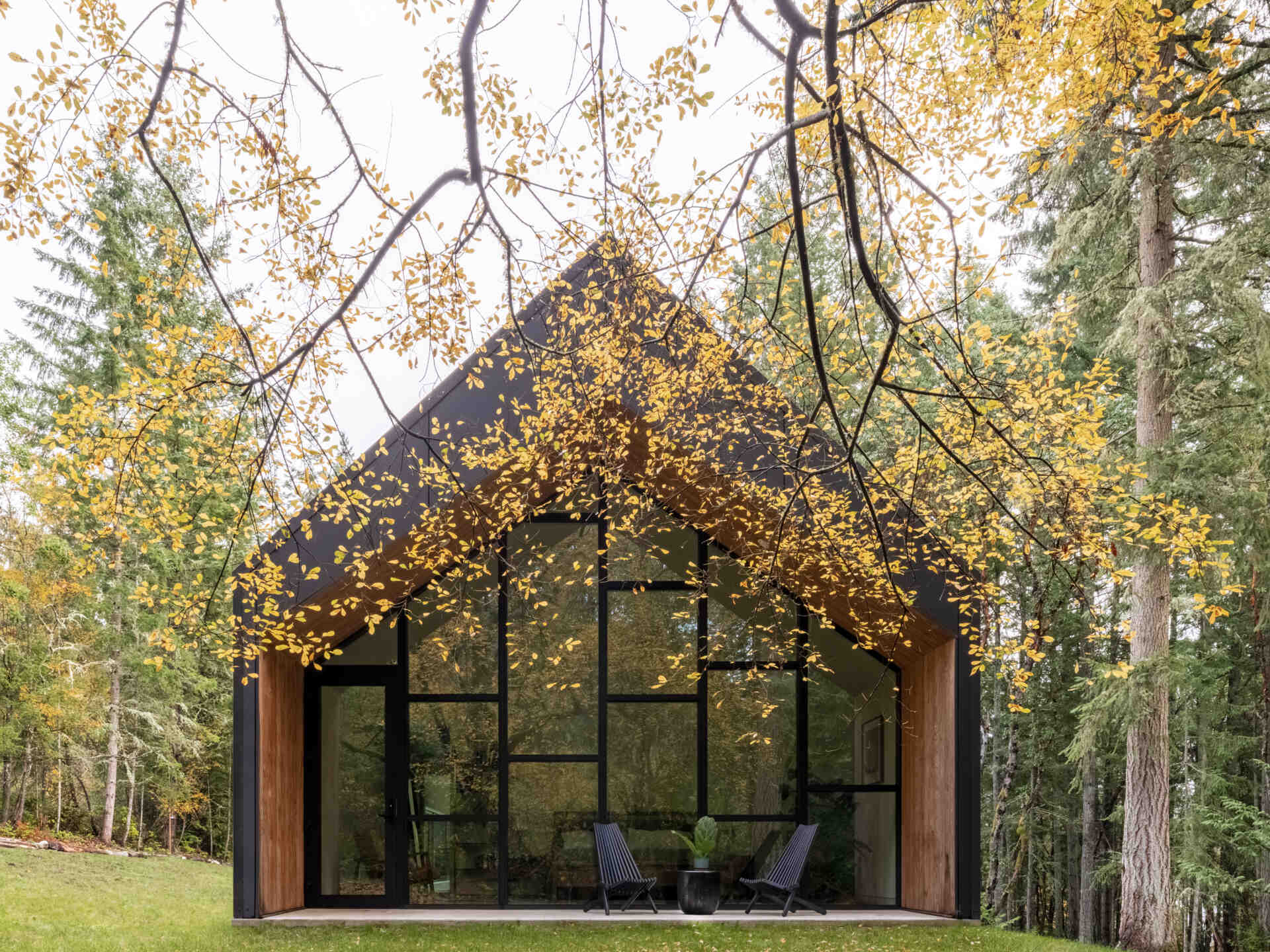 This modern gabled house on Vashon Island features black standing-seam metal, recessed timber walls, floor-to-ceiling glass, and a narrow footprint designed to preserve the surrounding forest.