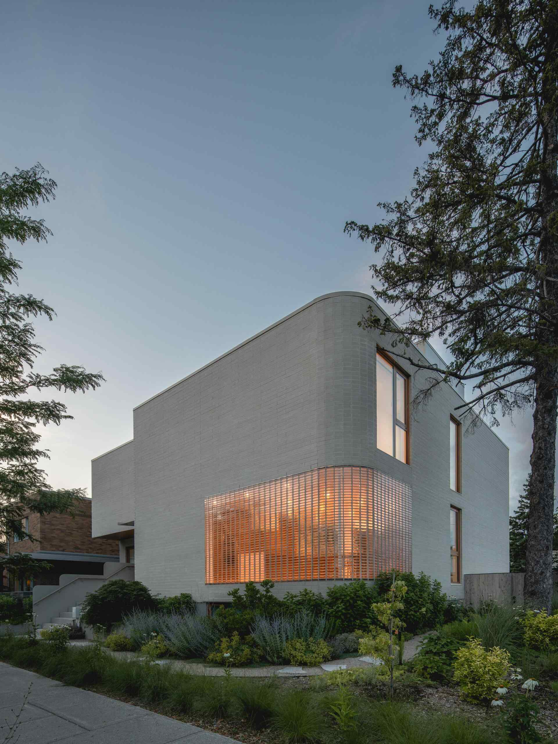 Explore the contemporary façade of The Lens in Montreal, designed by MU Architecture. Pale beige brick, rounded architectural details, a curved glass-brick wall, and lush landscaping create a private modern family home.
