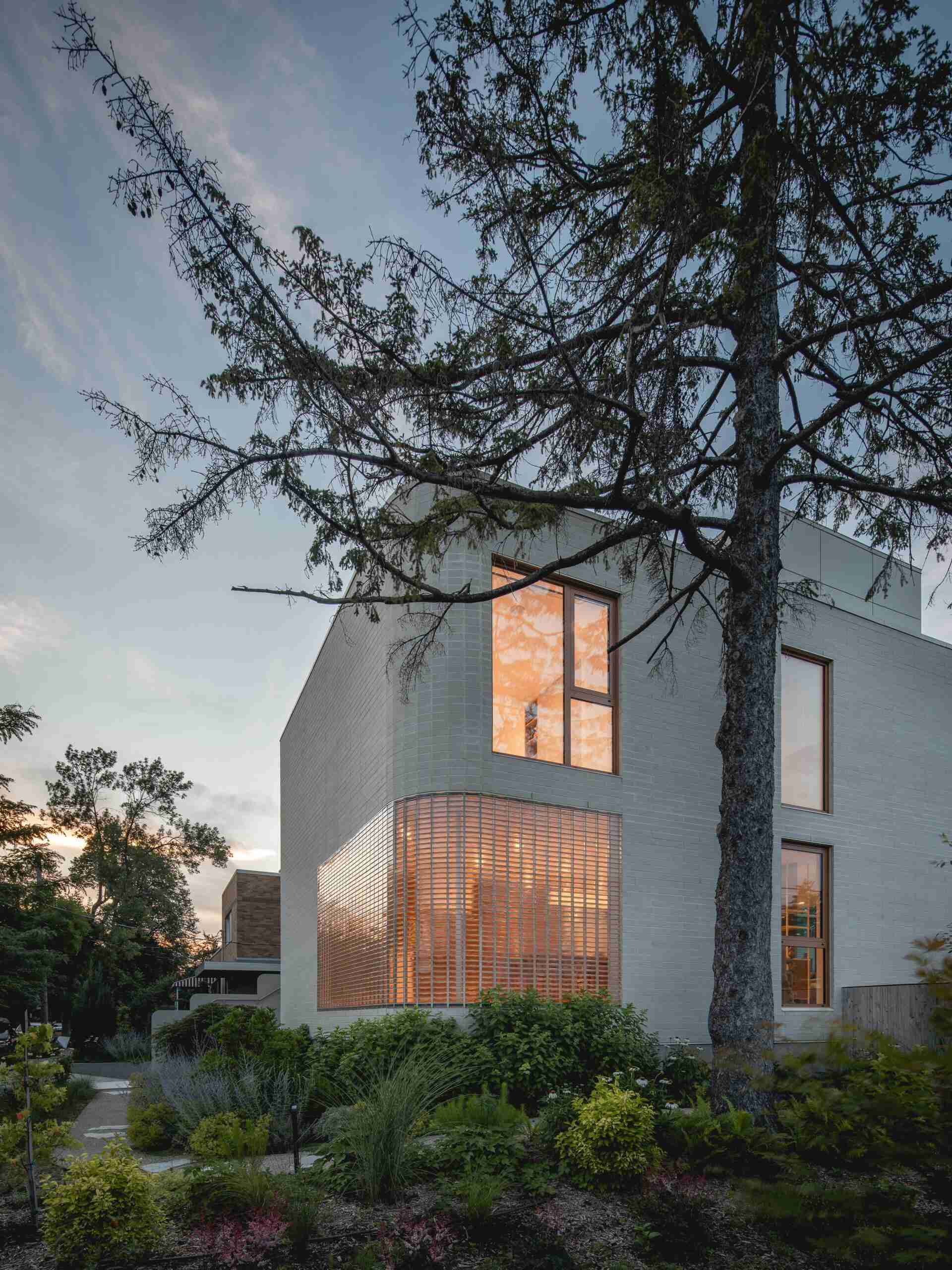 Explore the contemporary façade of The Lens in Montreal, designed by MU Architecture. Pale beige brick, rounded architectural details, a curved glass-brick wall, and lush landscaping create a private modern family home.