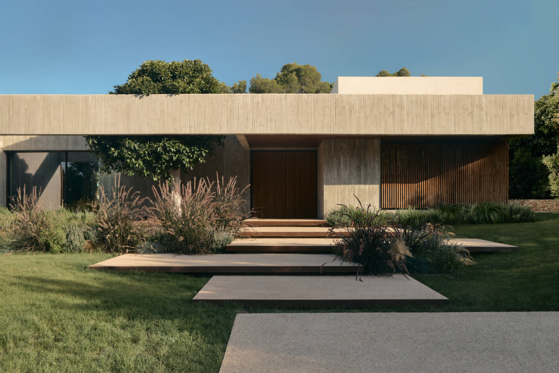 This modern concrete home by Viruta Lab in Valencia, Spain, features an L-shaped floor plan, board-marked concrete walls, horizontal architecture, and landscaped gardens.