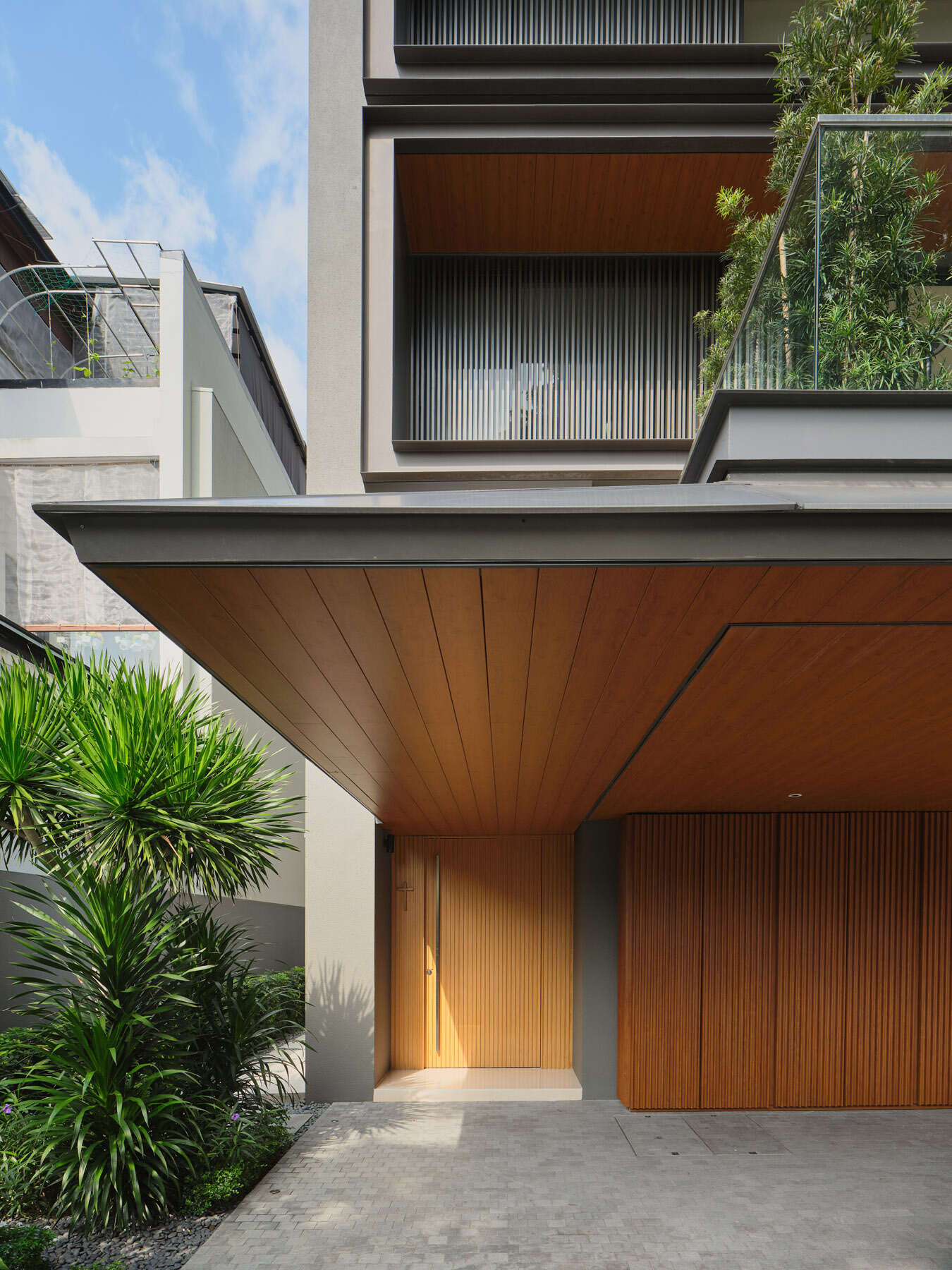 Step inside the entrance of JS-House, where a timber-lined porch leads to a double-height foyer with vertical wood panelling, sculptural lighting, and natural light.