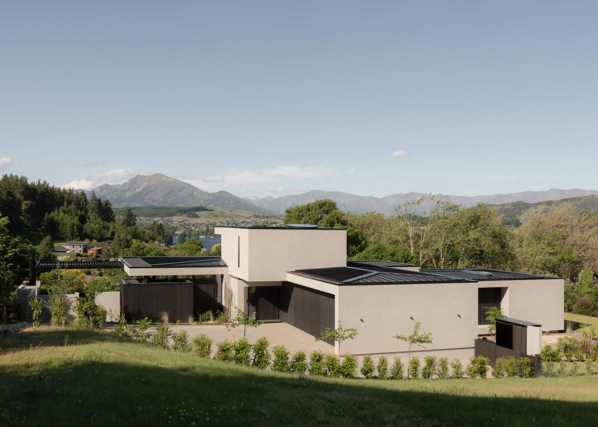 A contemporary house in W?naka, New Zealand, designed by Condon Scott Architects, featuring a cantilevered upper level, pale plaster exterior, black wood cladding, and modern geometric architecture.