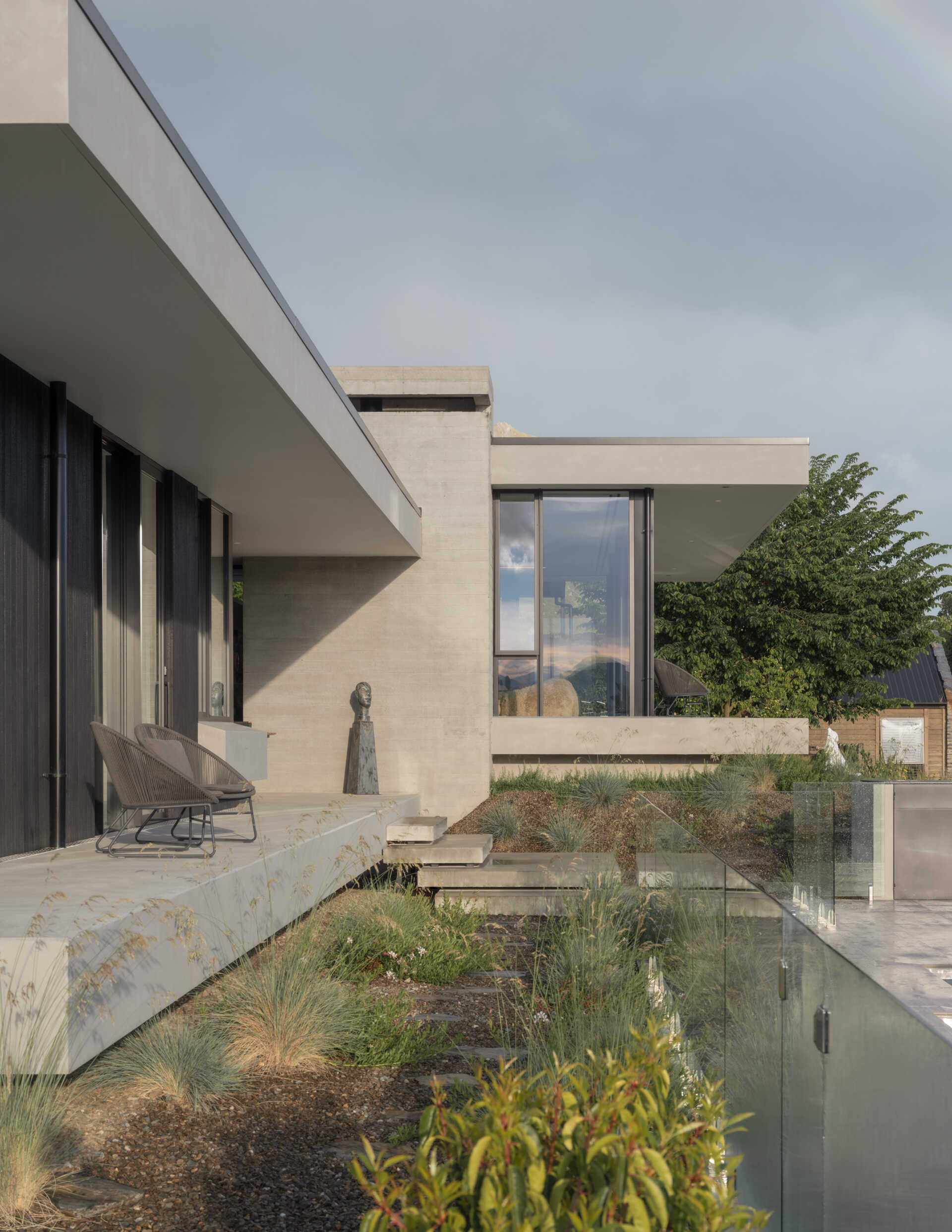 Explore a contemporary hillside house in W?naka featuring stepped architecture, floating concrete terraces, floor-to-ceiling windows, mountain views, and landscaped gardens with sculptural artworks.